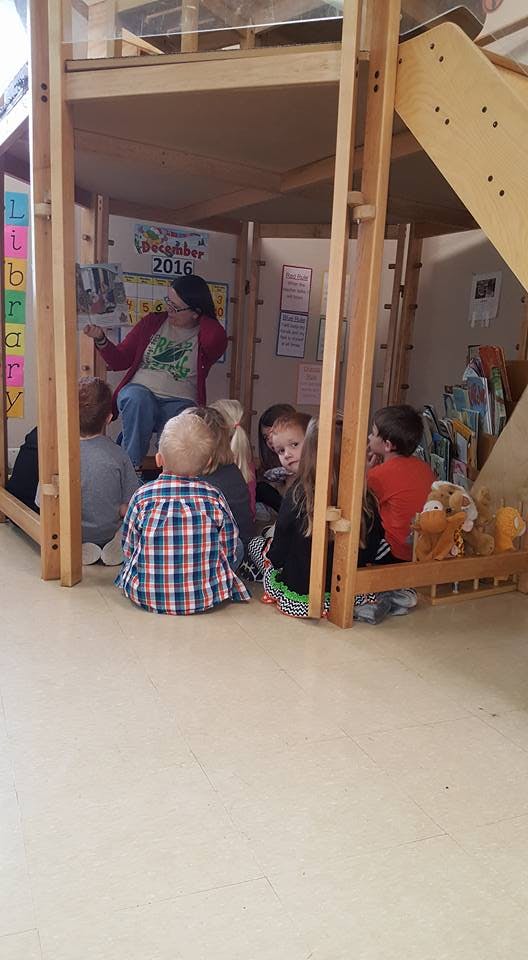 Adult reading to children in a wooden play structure
