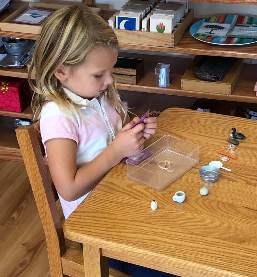 Child sitting at a table, holding small objects