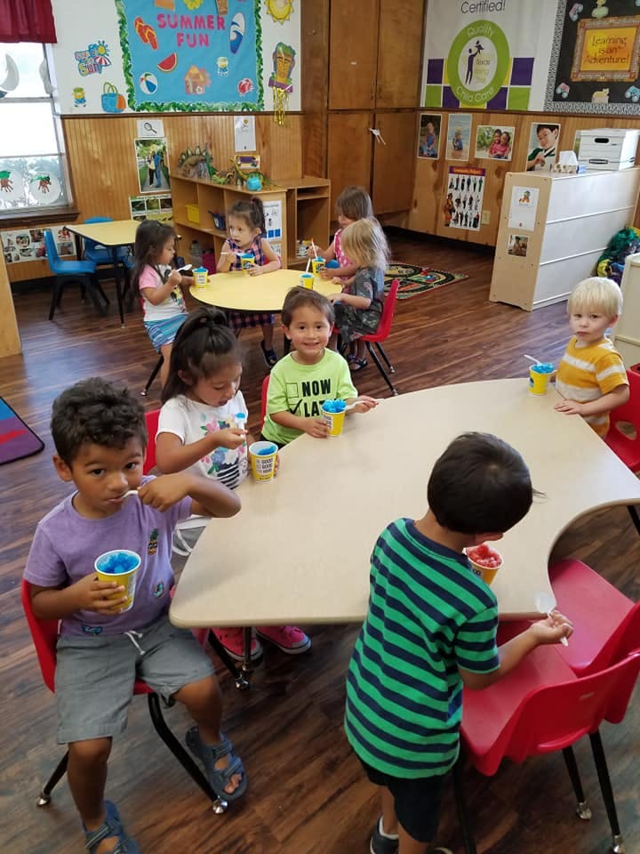 Children sitting at tables in a classroom, eating from cups