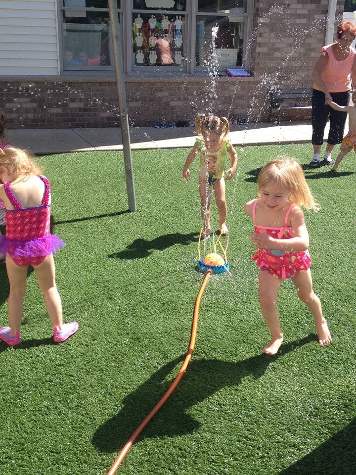 Children playing in a sprinkler on artificial grass