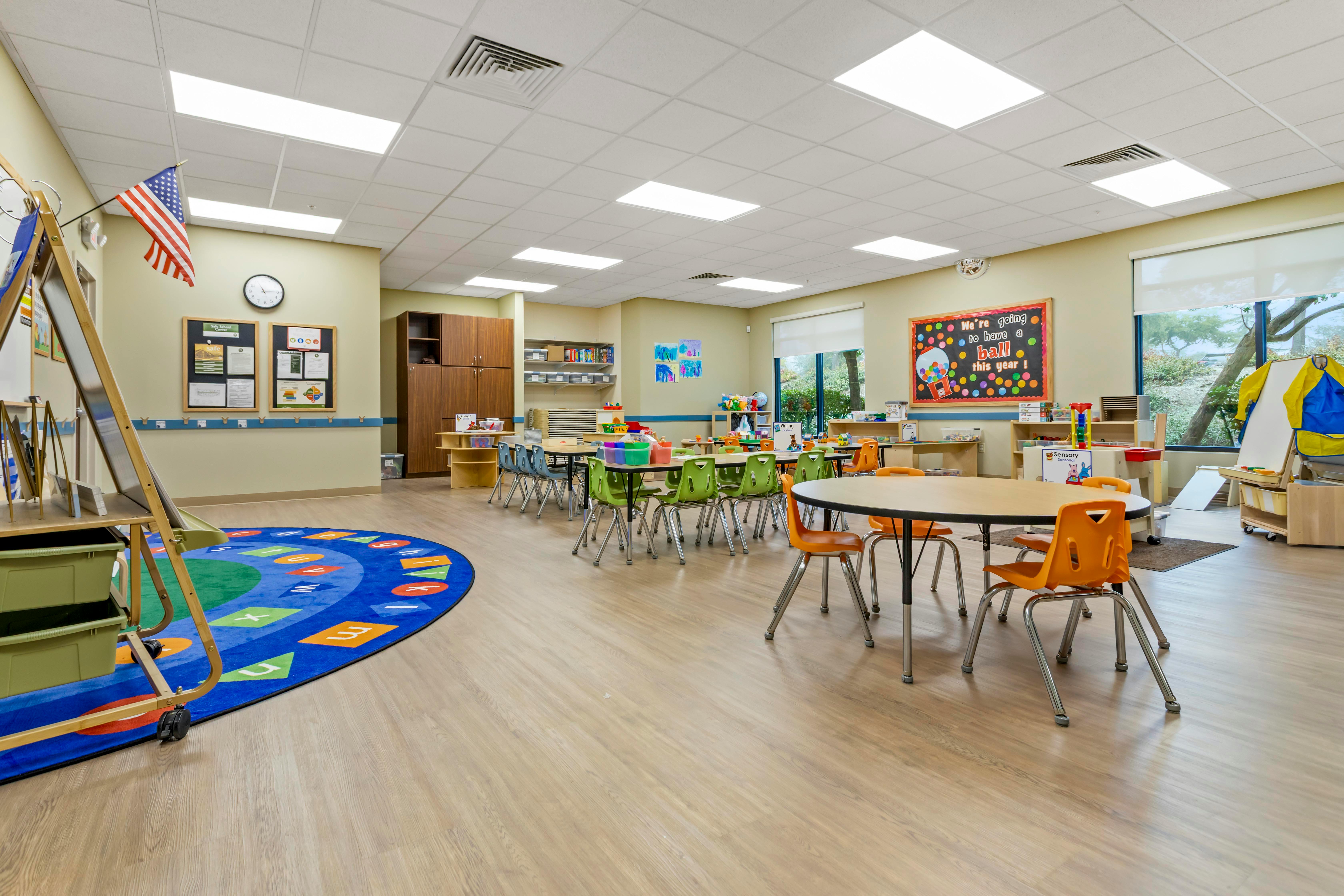 Classroom with small tables and chairs, ABC rug, and bulletin boards