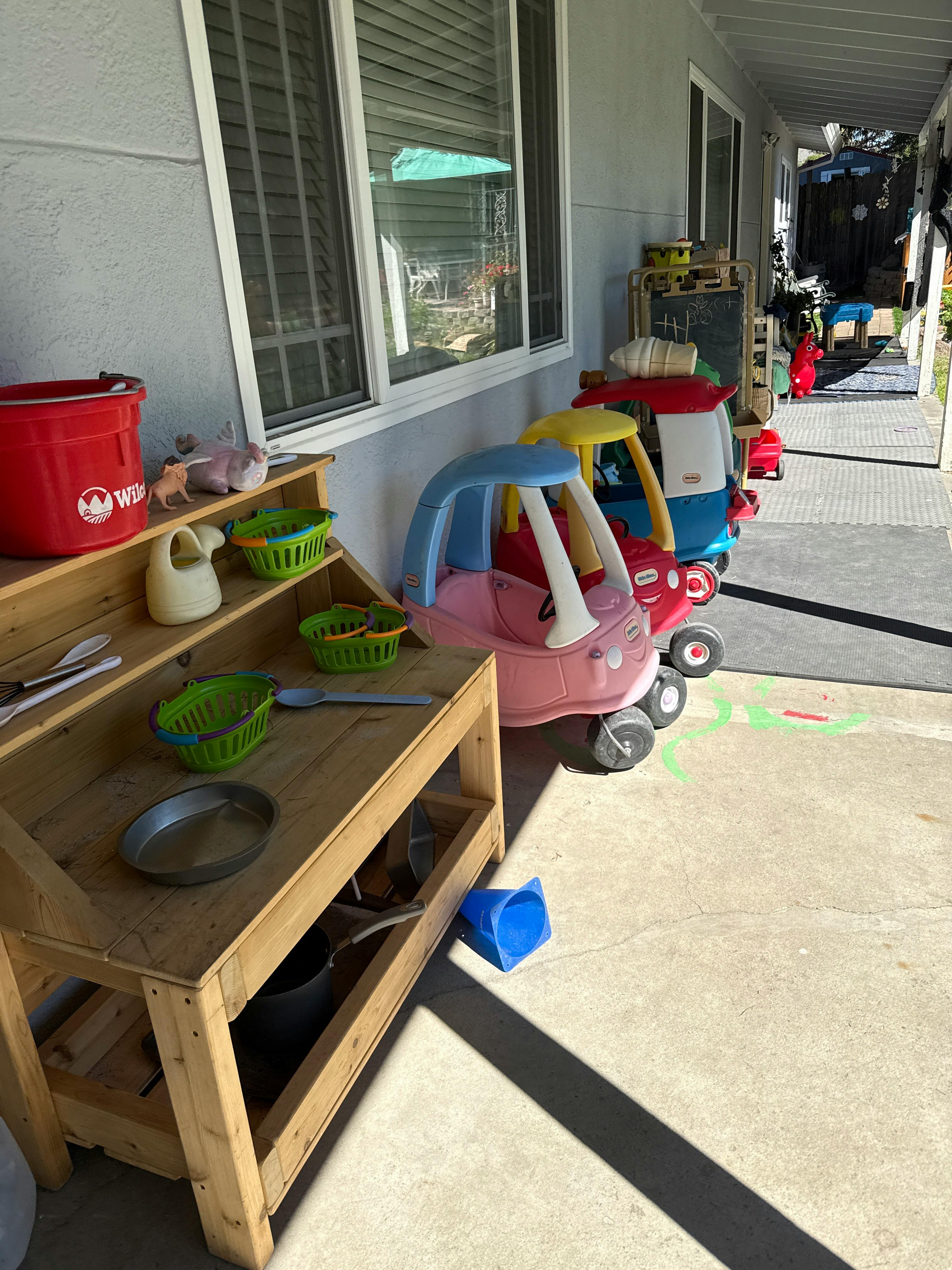 Children's play area with plastic ride-on toys, a chalkboard, and a wooden play kitchen