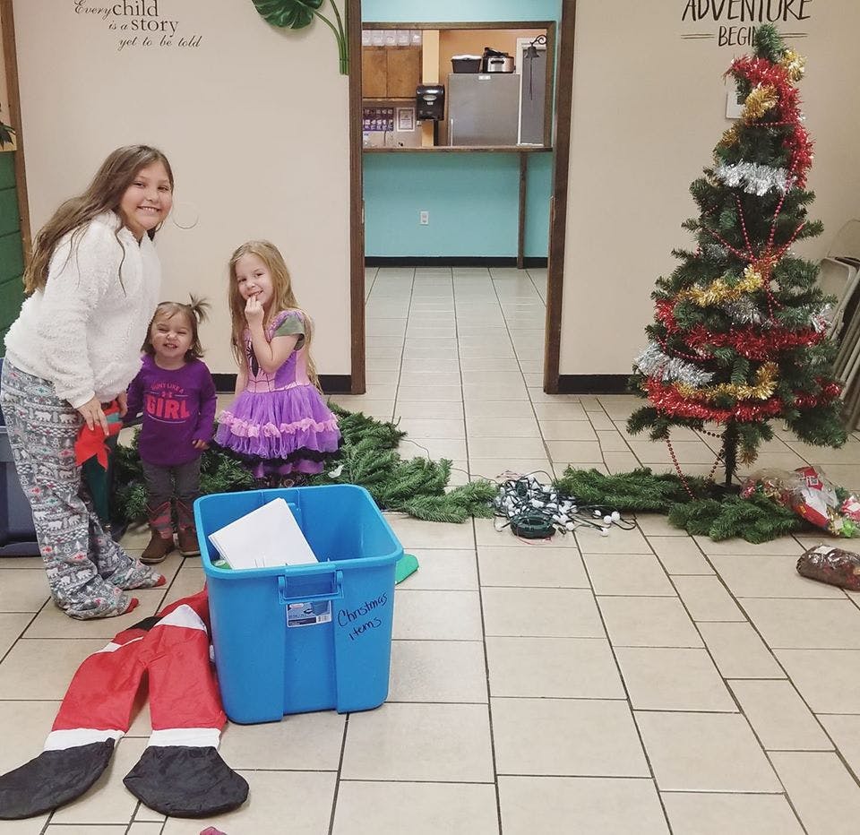 Three children standing near a partially decorated Christmas tree