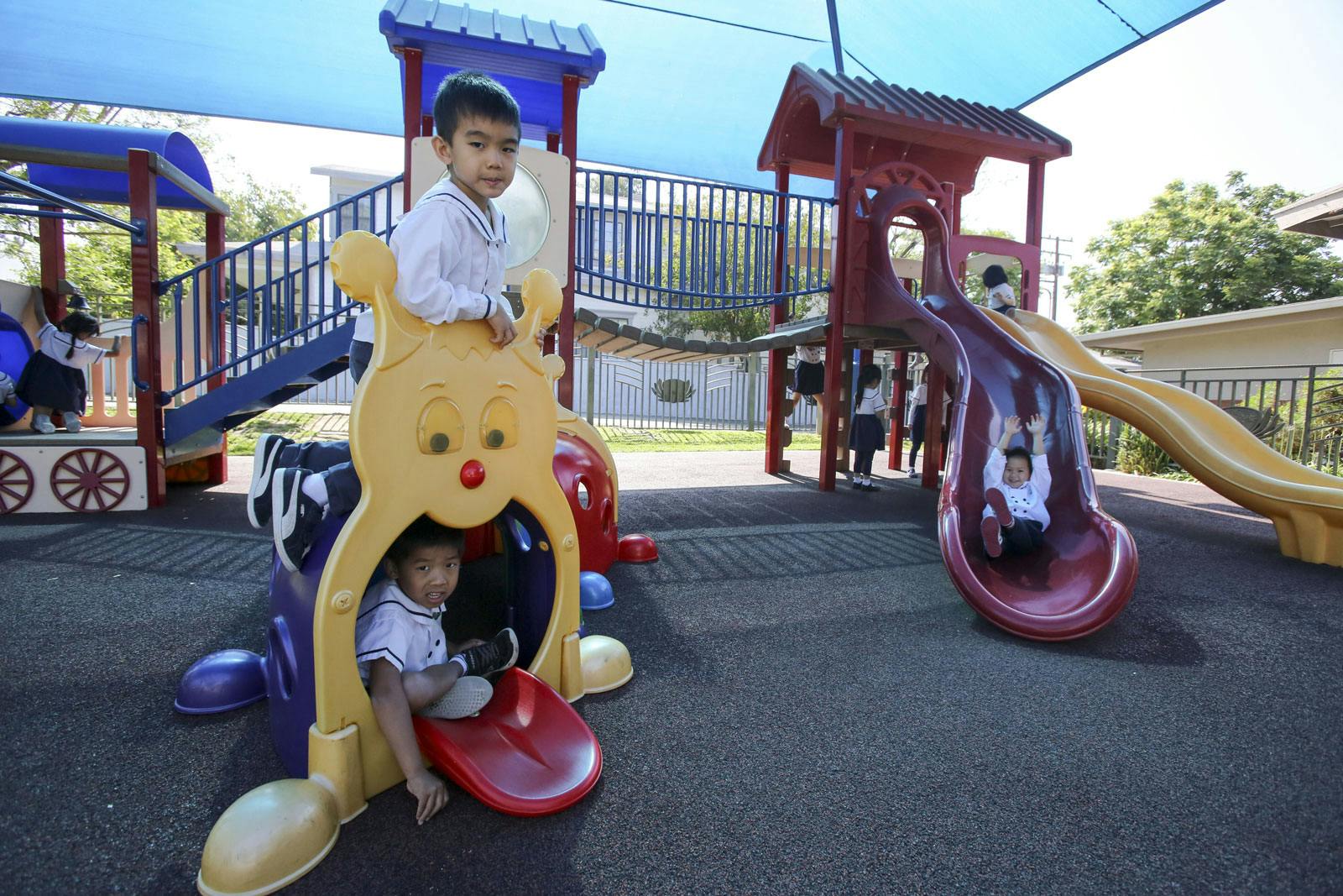 Children playing on playground equipment, one on a slide, two on a climbing structure