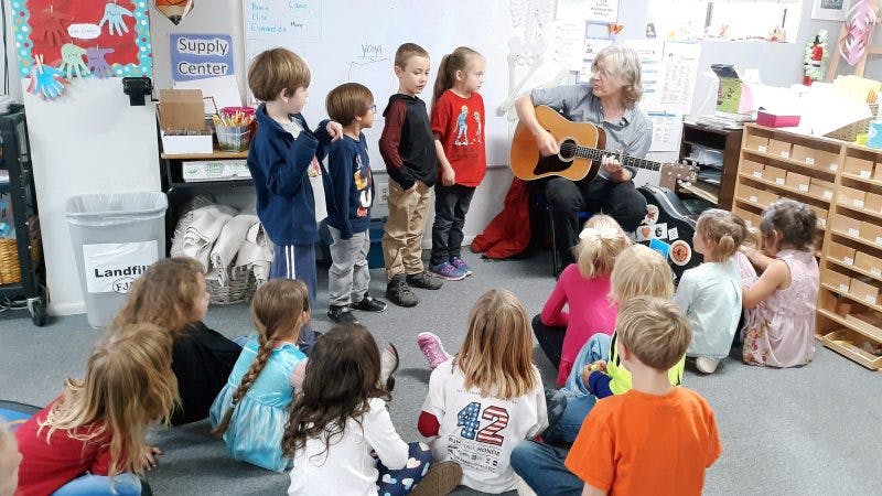 Adult playing guitar for children in a classroom