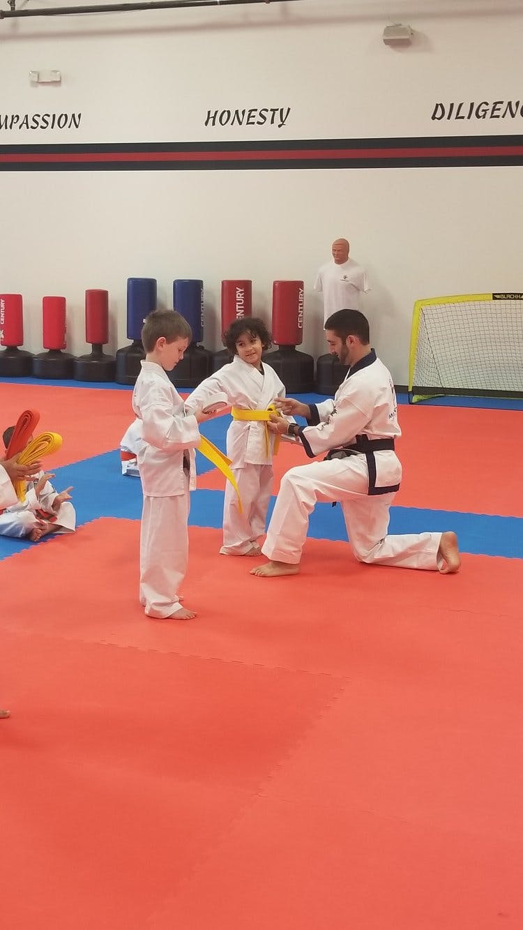 Adult helping child with yellow belt in martial arts class