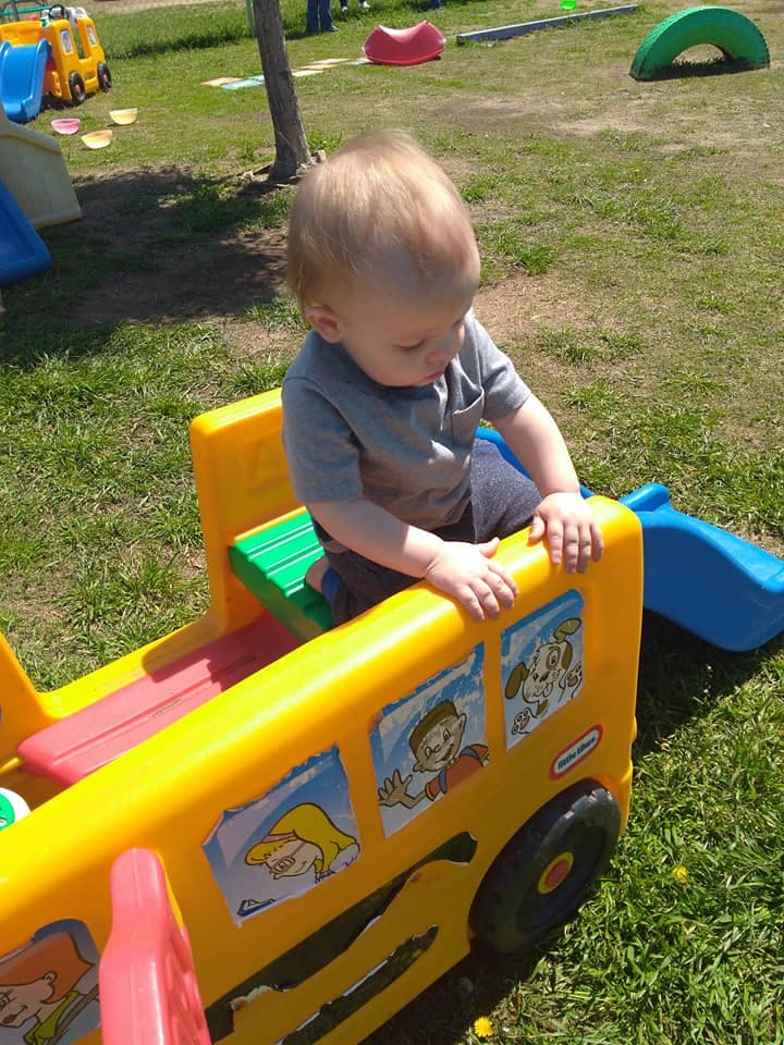 Child playing in a yellow toy bus on grass