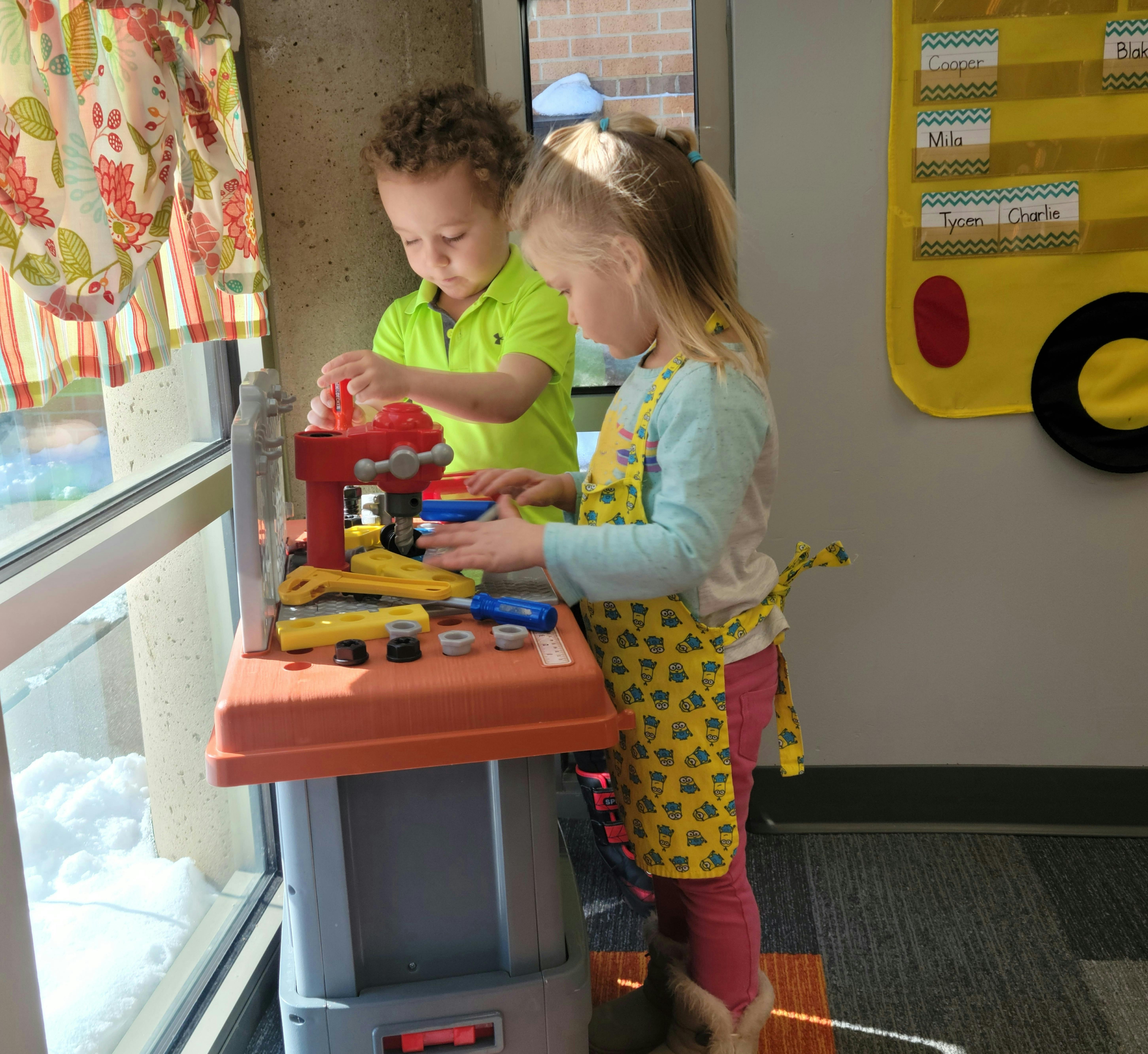 Two children playing with a toy workbench