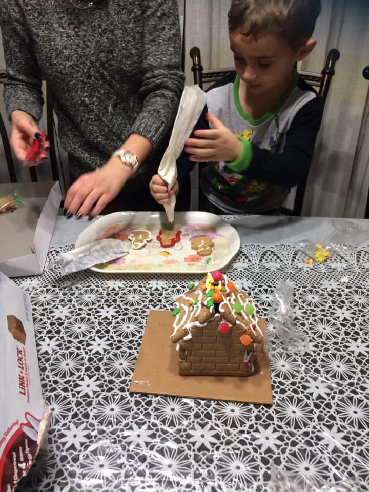 Person and child decorating cookies with icing, gingerbread house in foreground