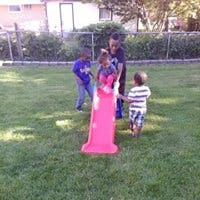 Four children playing on a pink slide in a grassy area
