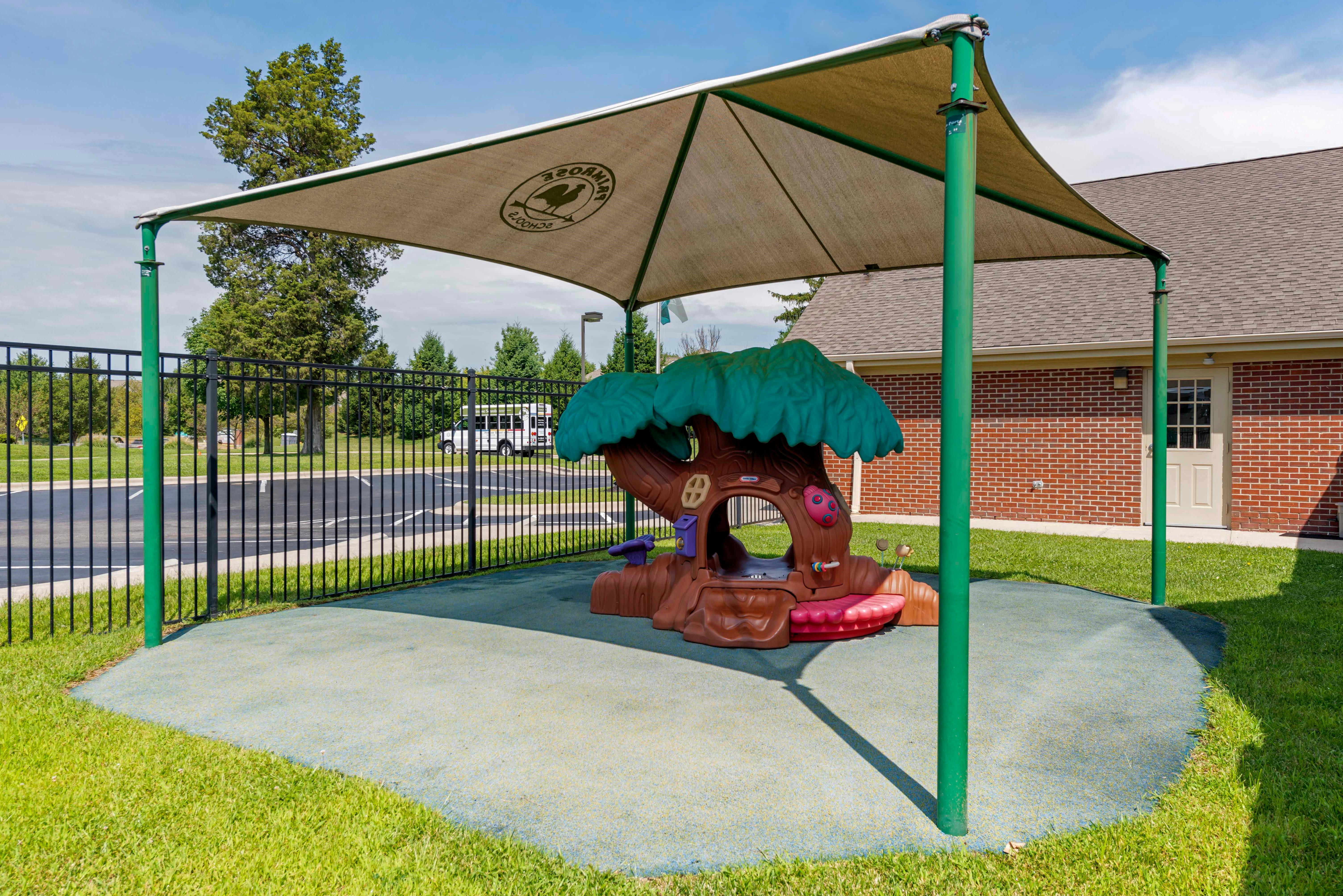 Playground with a treehouse-shaped play structure under a large shade canopy