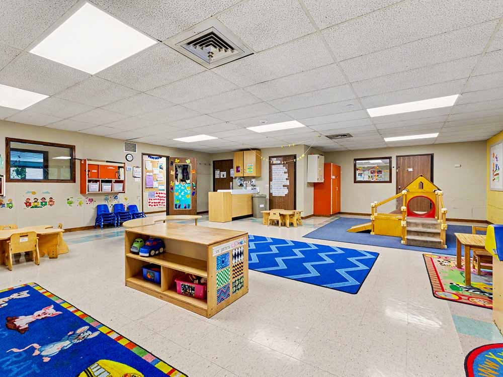 An empty daycare classroom with toys, tables, and a small play structure