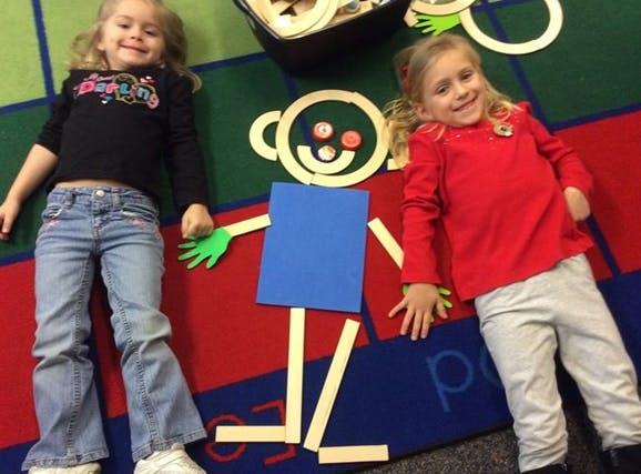 Two children lying on a colorful rug next to a craft person figure