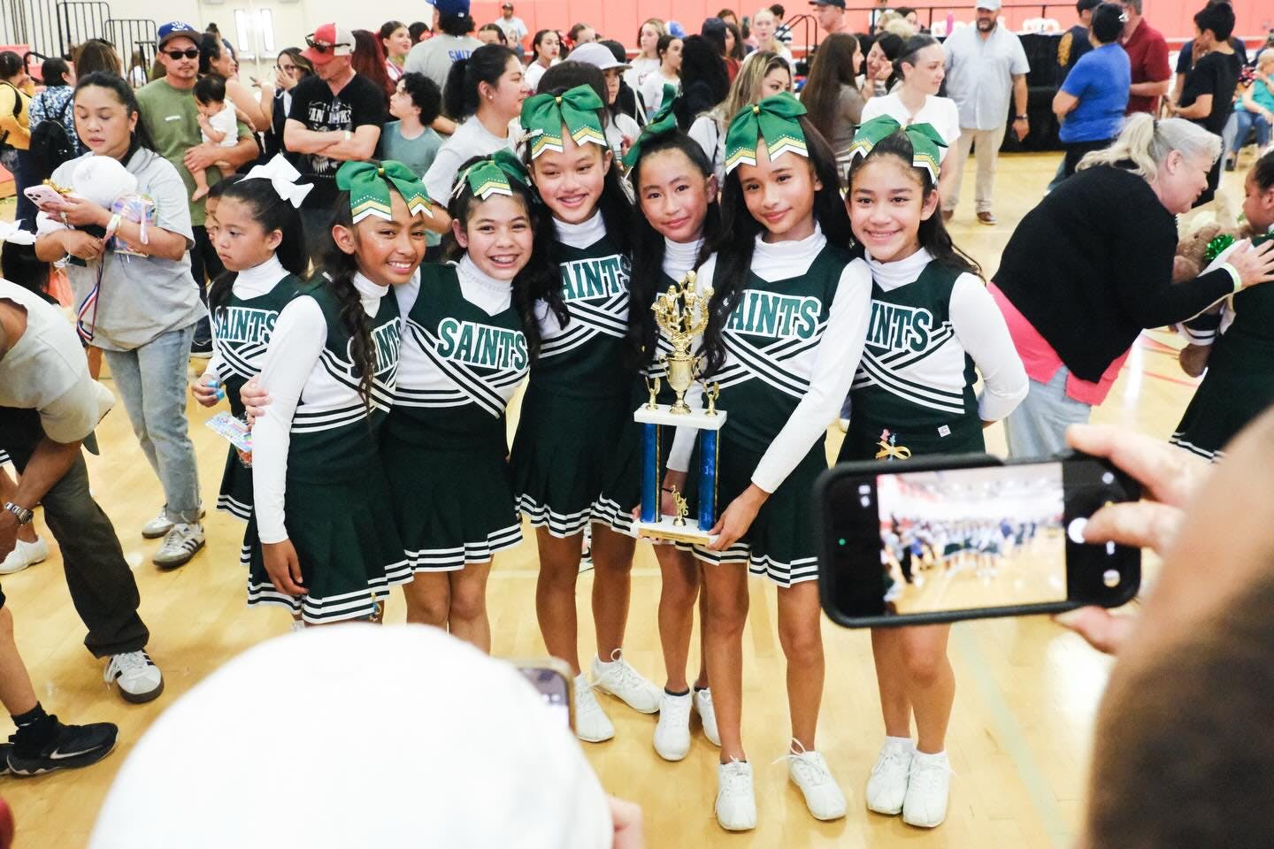 Group of children in Saints cheerleading uniforms posing with a trophy