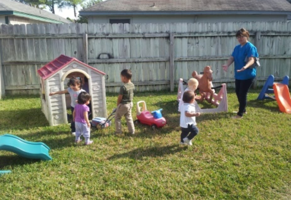 Children playing in a grassy yard with a person standing nearby