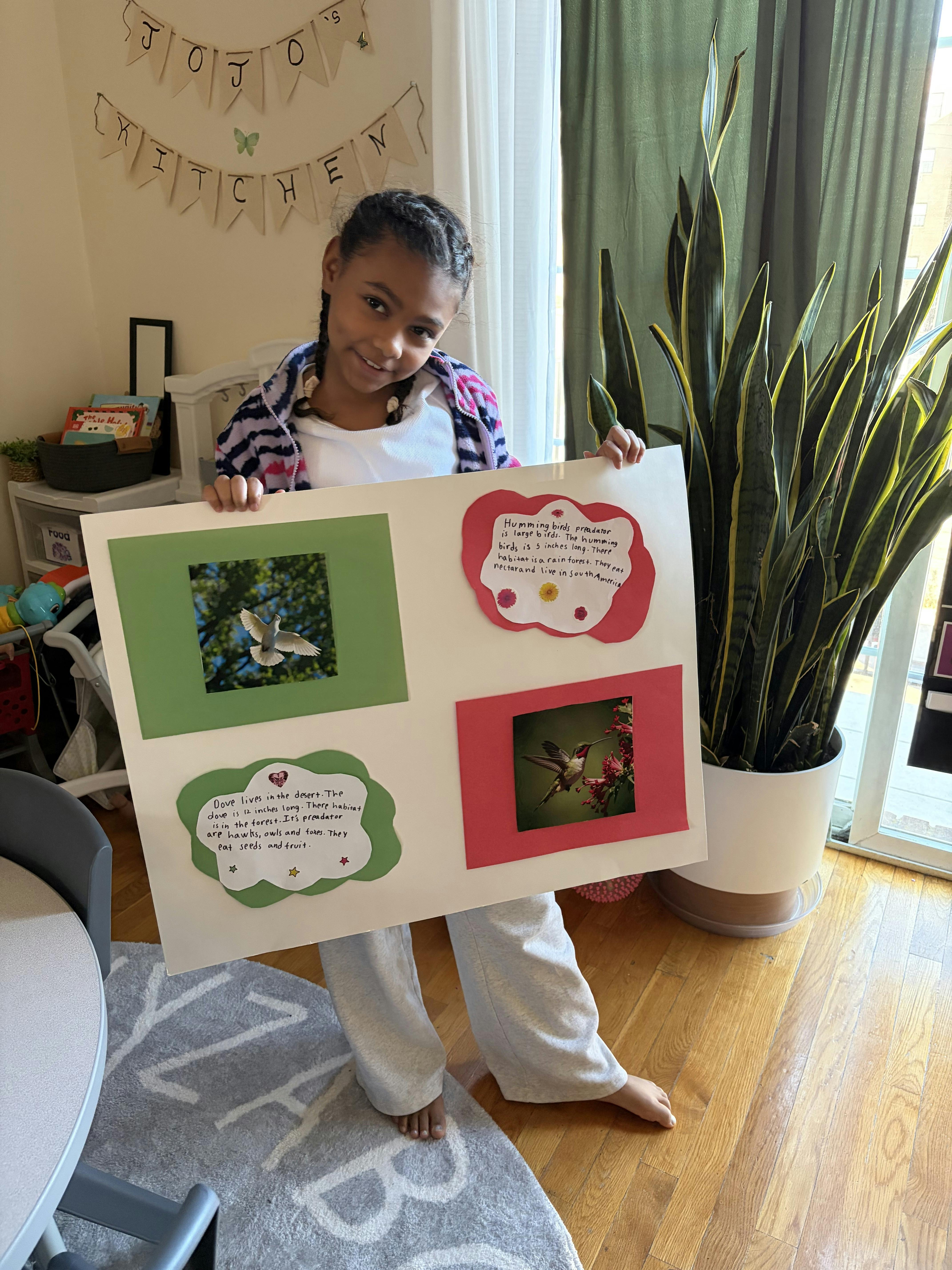 Child standing and holding up a science project board with bird pictures