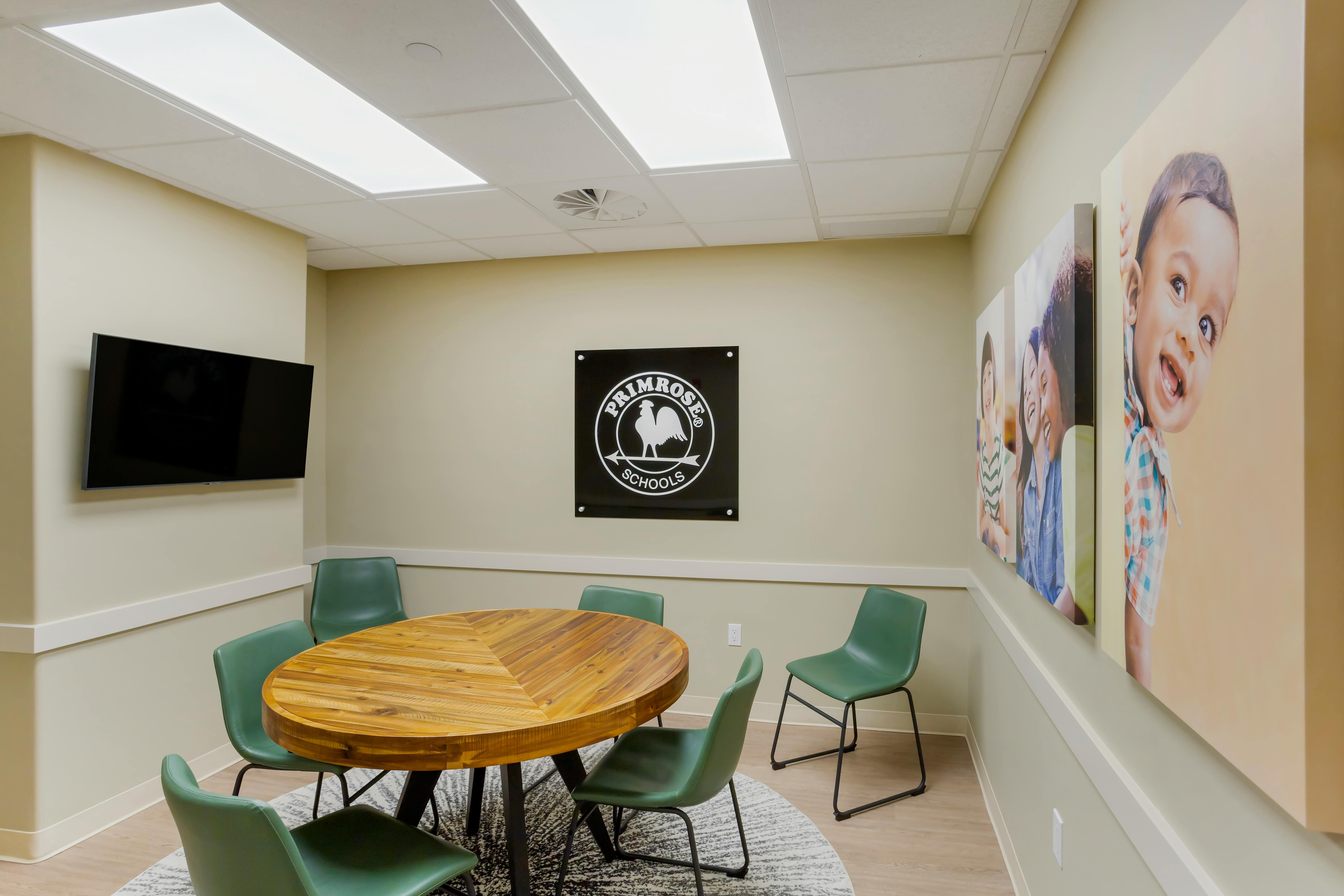 Meeting room with round wood table and green chairs, Primrose Schools logo on wall