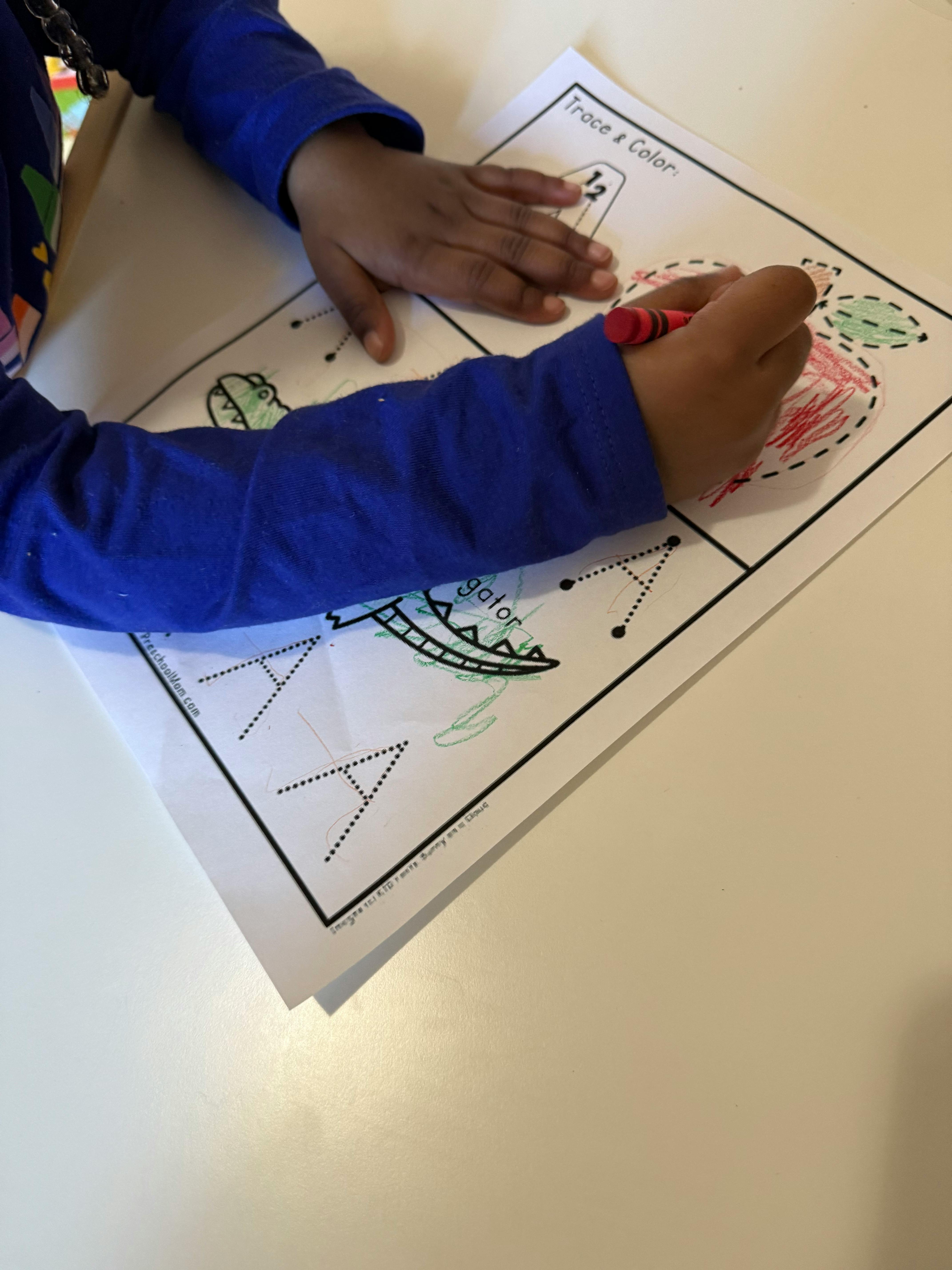 Child coloring a picture of an apple with a red crayon