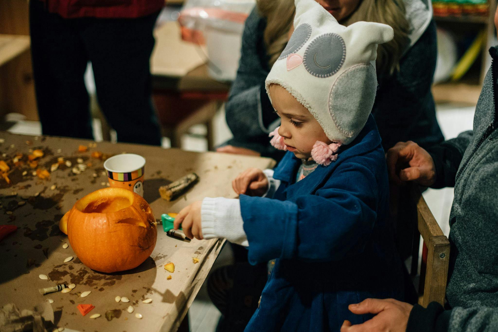 Child in an owl hat carving a pumpkin