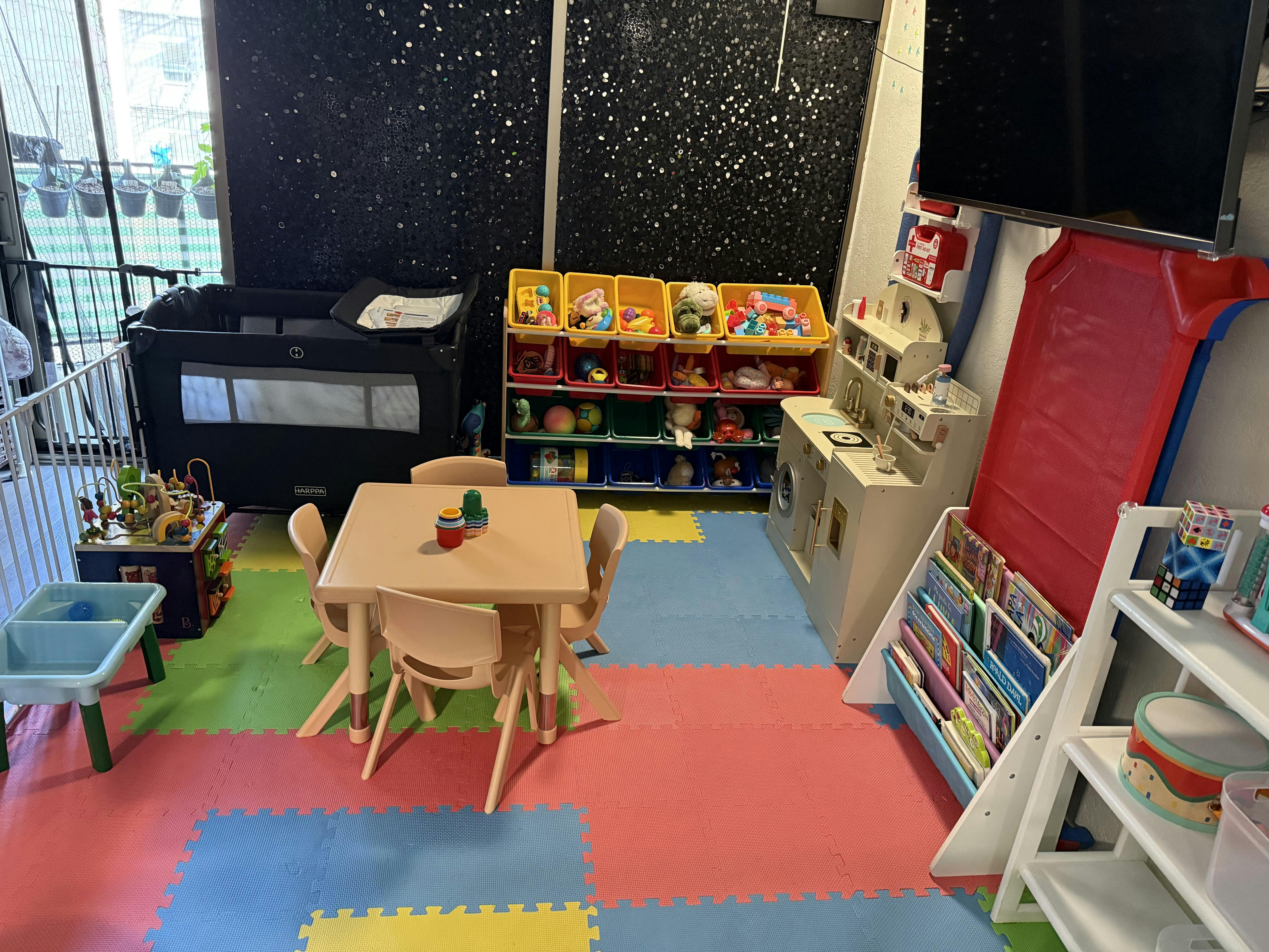 Child's playroom with colorful mats, a small table, toys, and a crib