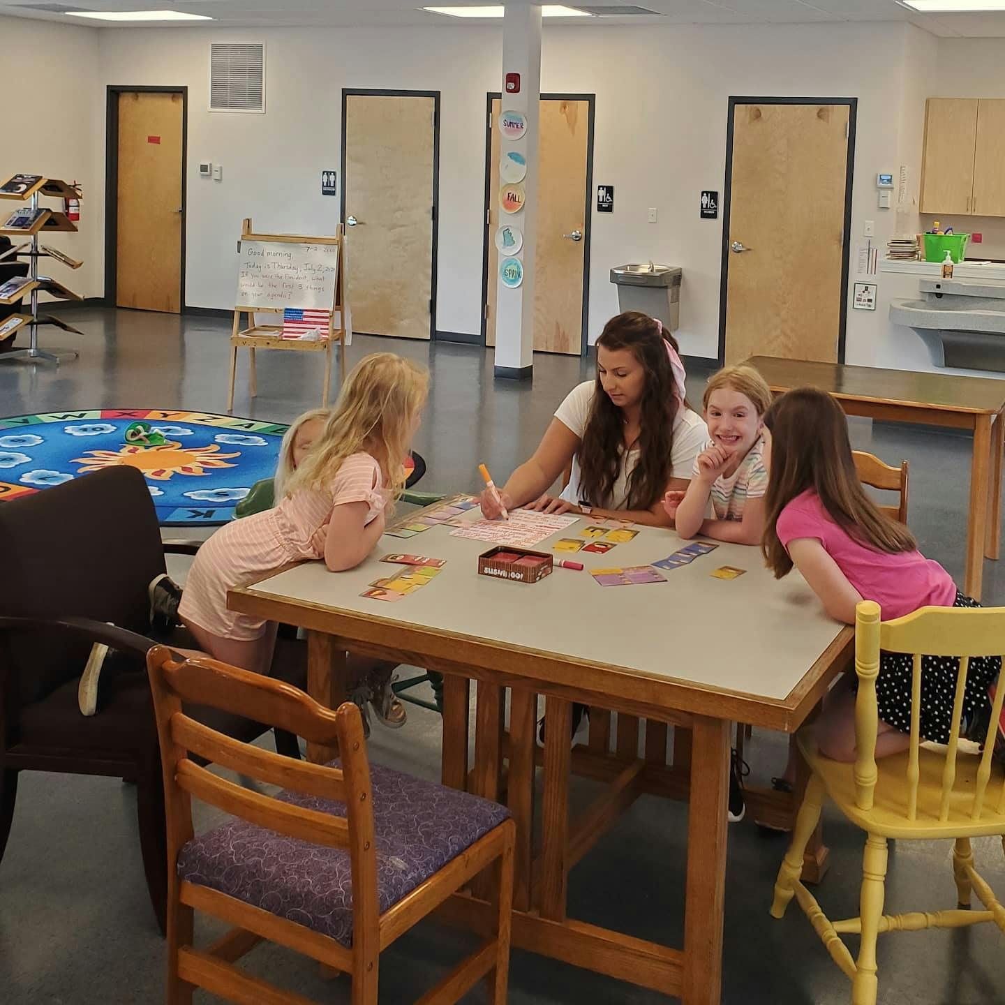 Person and three children sitting at a table with papers and drawing