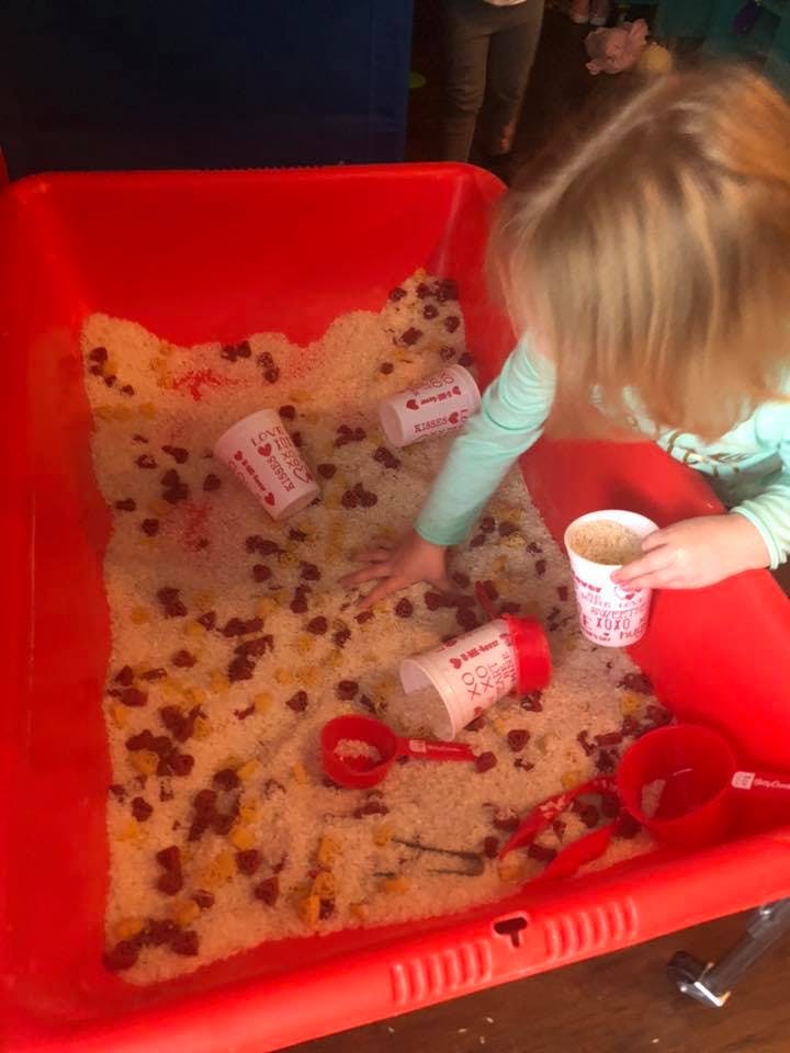 Child playing with rice and beans in a red bin