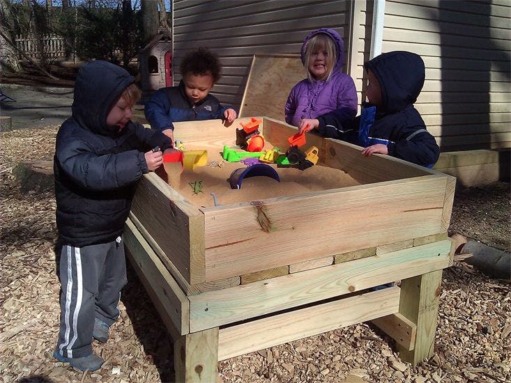 Children playing in a wooden sandbox with toys