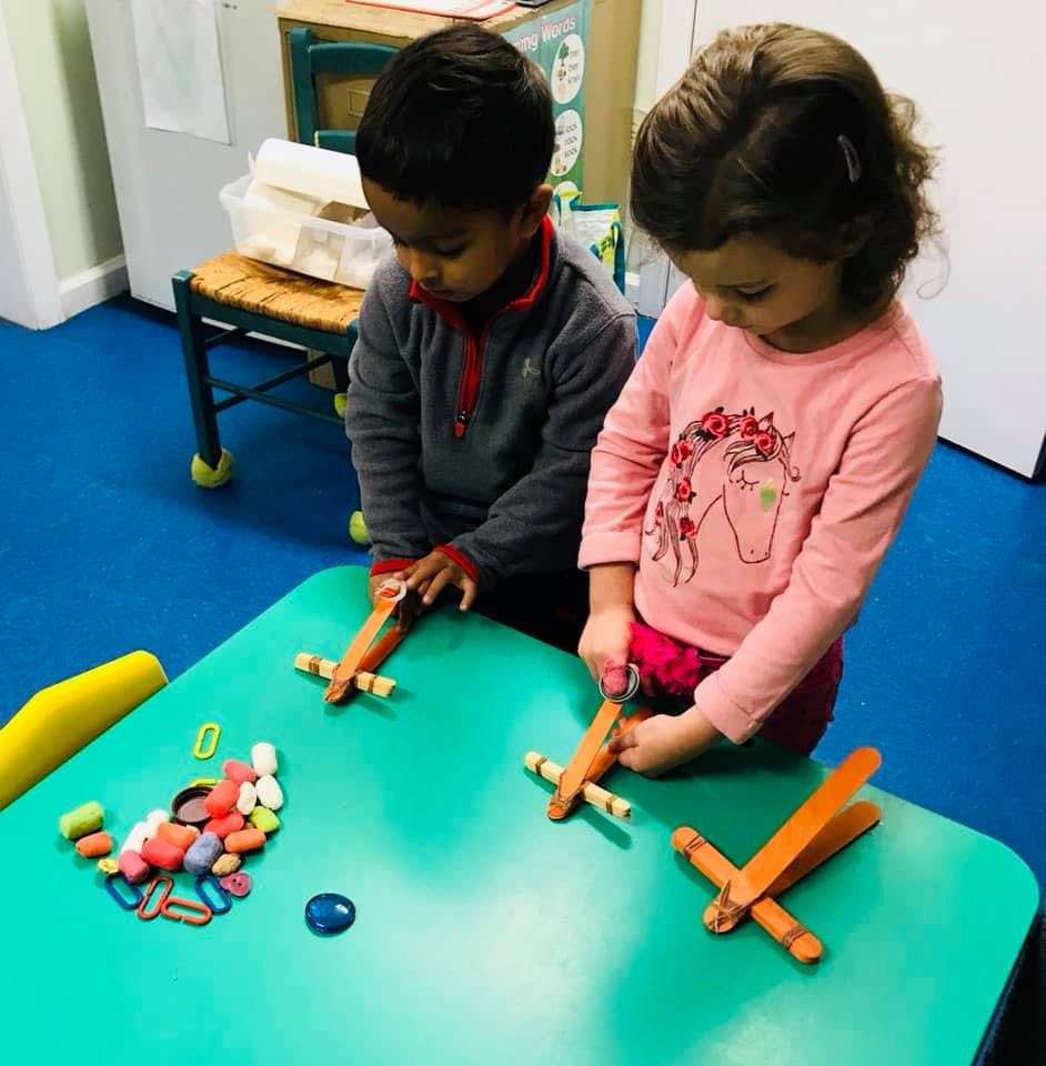 Two children playing with wooden airplanes on a green table