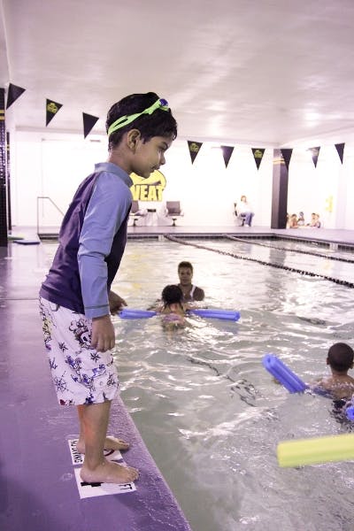 Child in swim goggles standing at the edge of a swimming pool