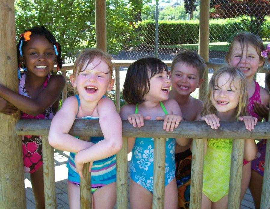 Group of children in swimsuits looking over a wooden fence