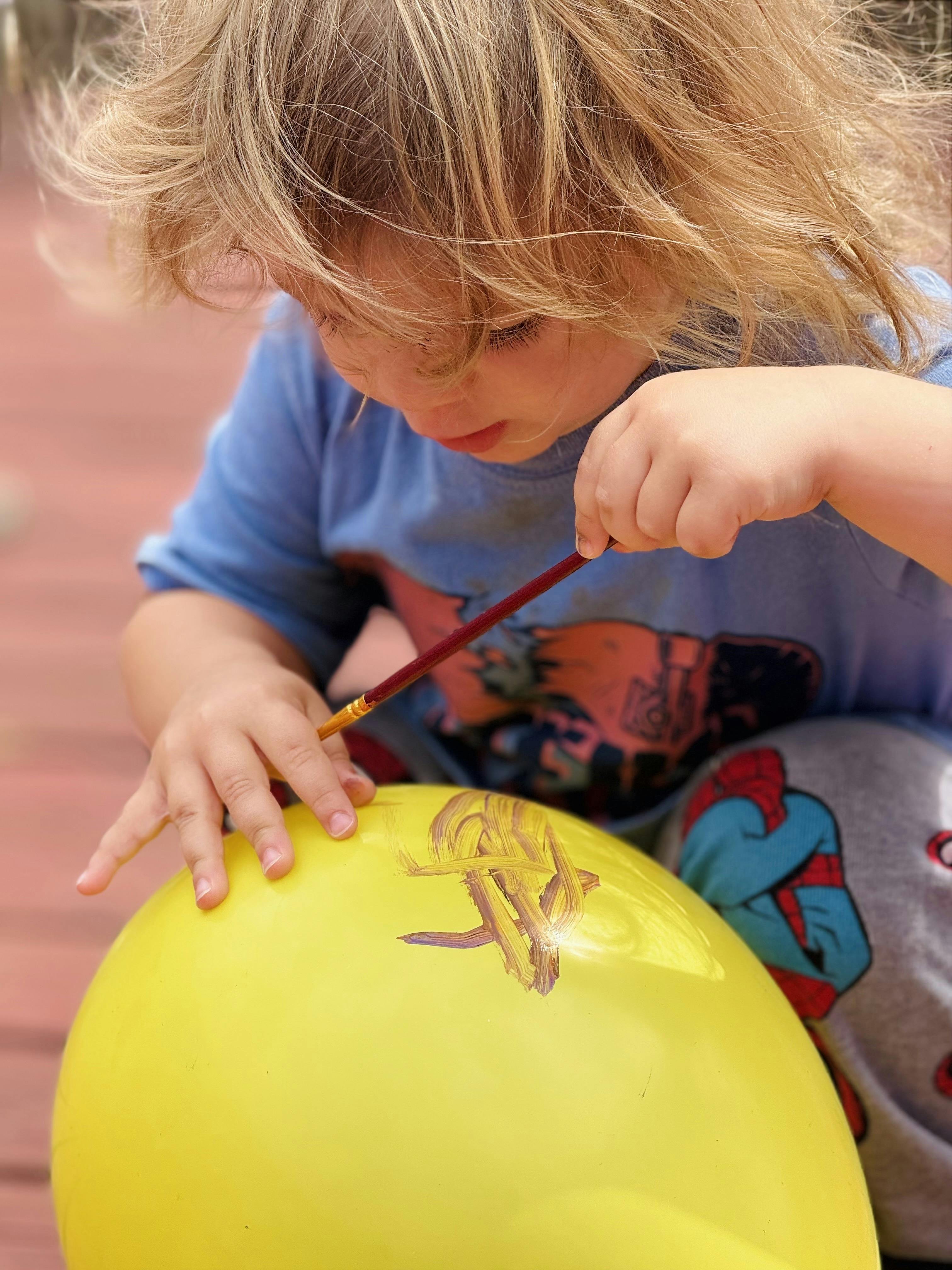 Child painting on a yellow balloon with a brush