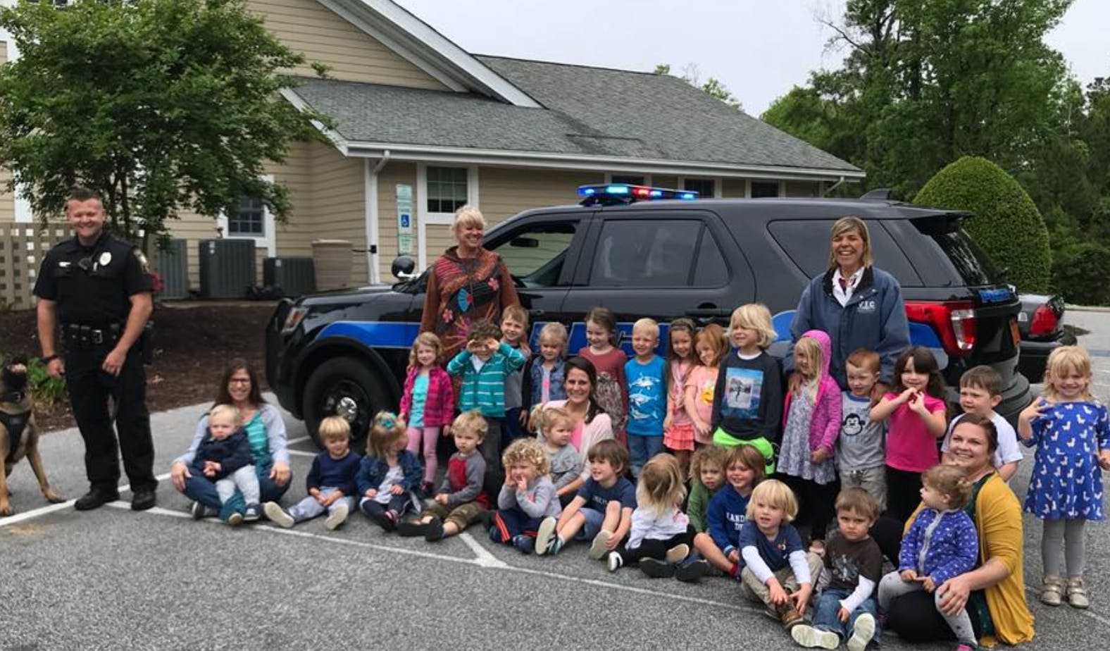 Police officer and adults with a group of children in front of a police vehicle