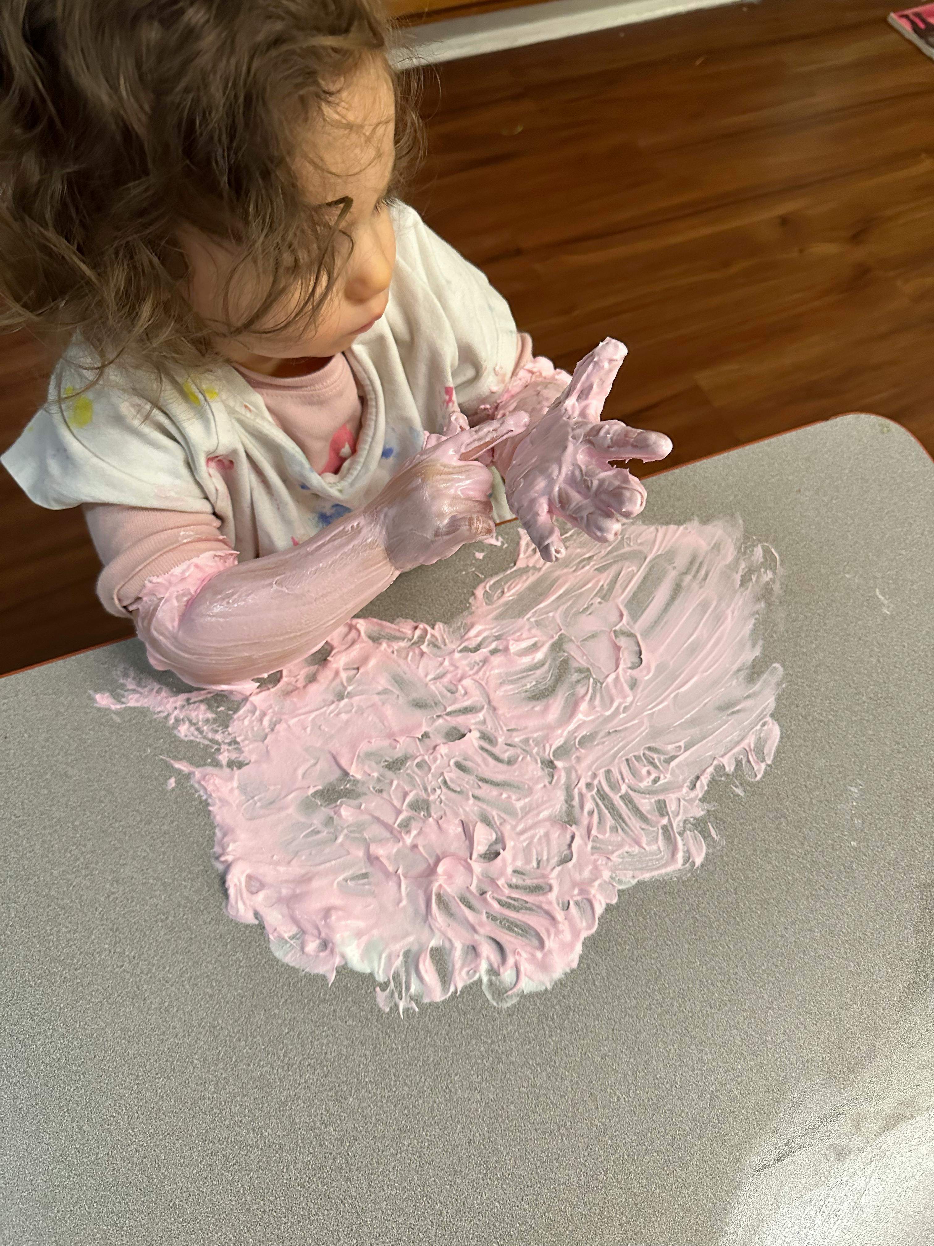 Child playing with pink paint or shaving cream on a table