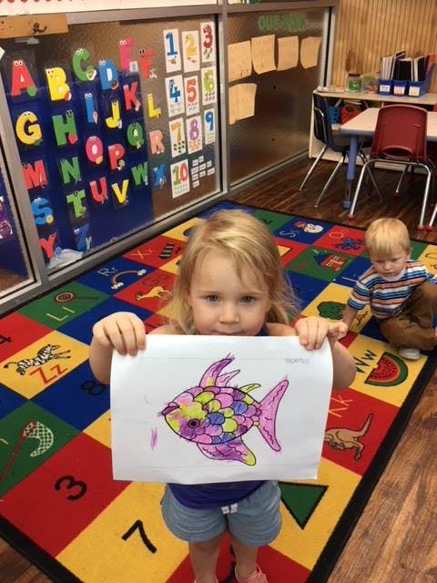 Child holding up a drawing of a colorful fish
