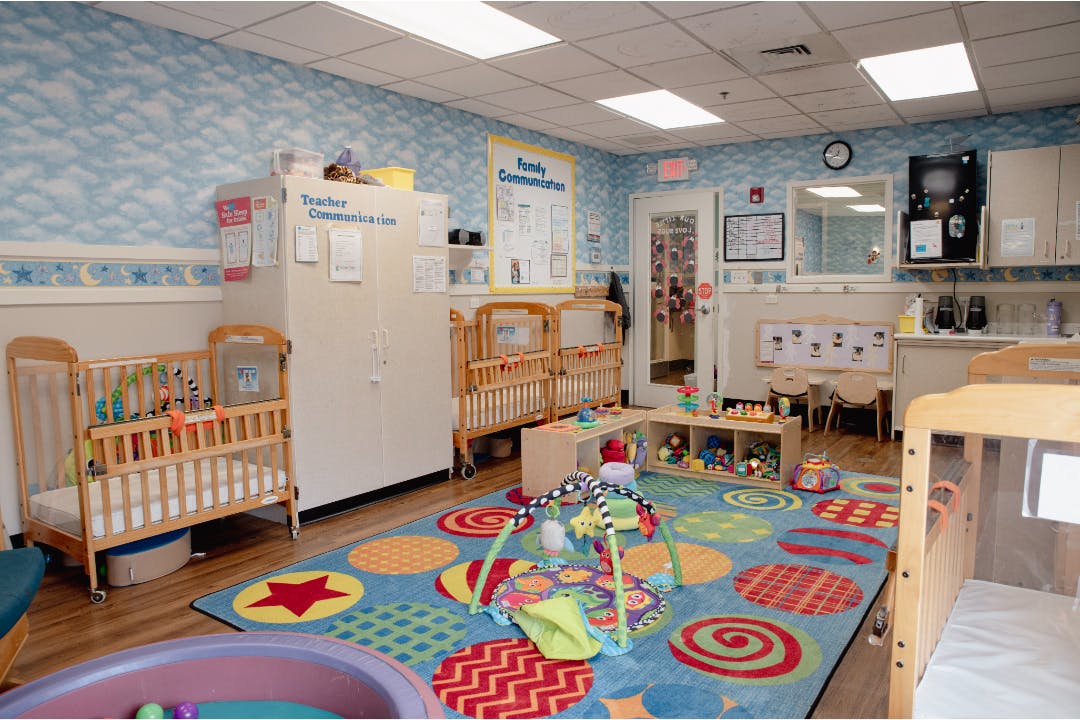 Classroom with multiple cribs, a colorful play rug, and child development materials