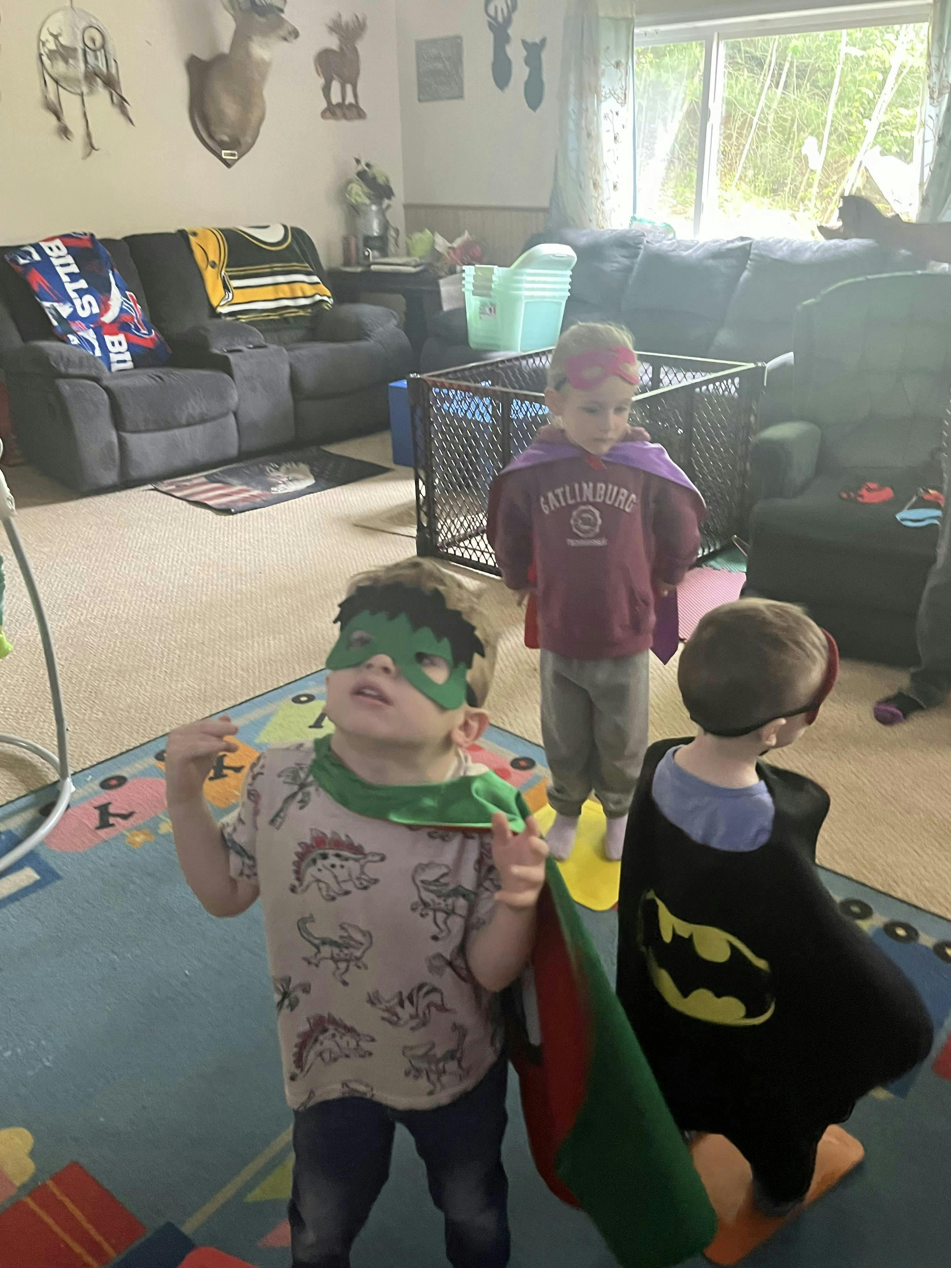 Three children in superhero costumes playing indoors