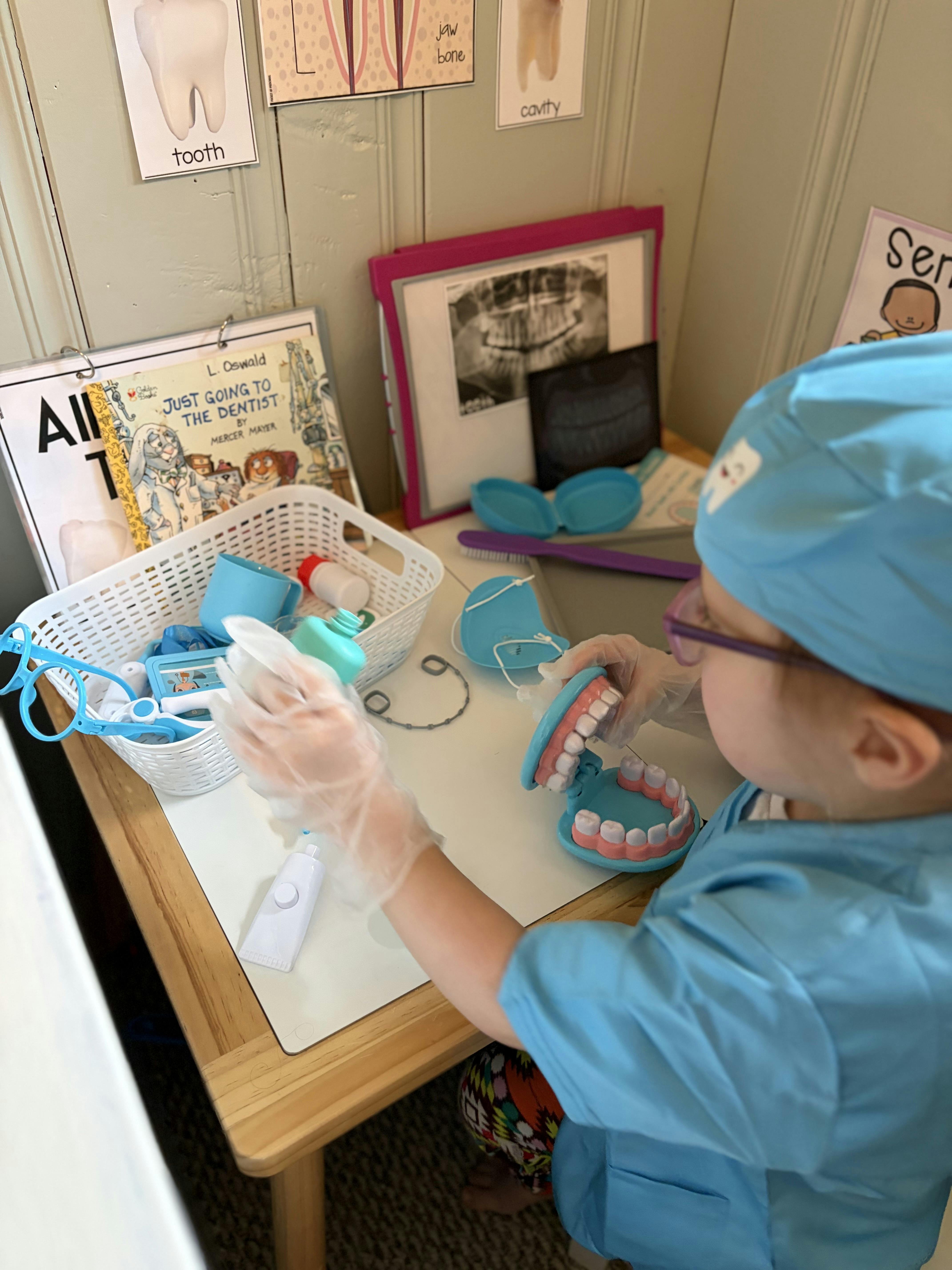 Child in scrubs and gloves playing with a dental model and toy toothpaste