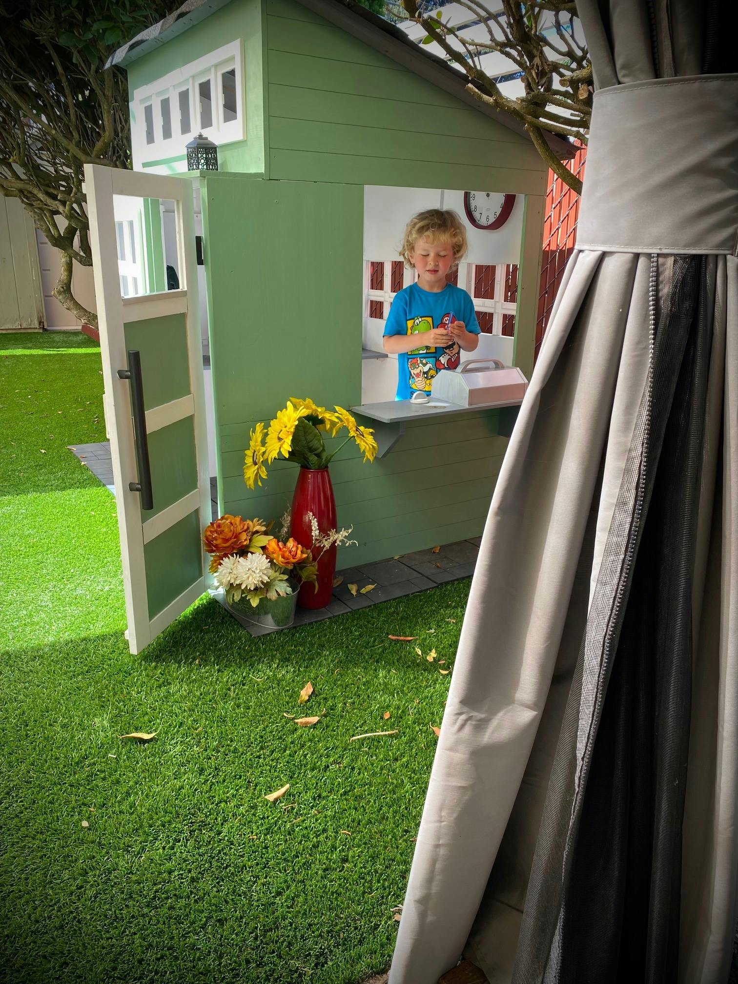 Child standing in a playhouse window with flowers on a counter