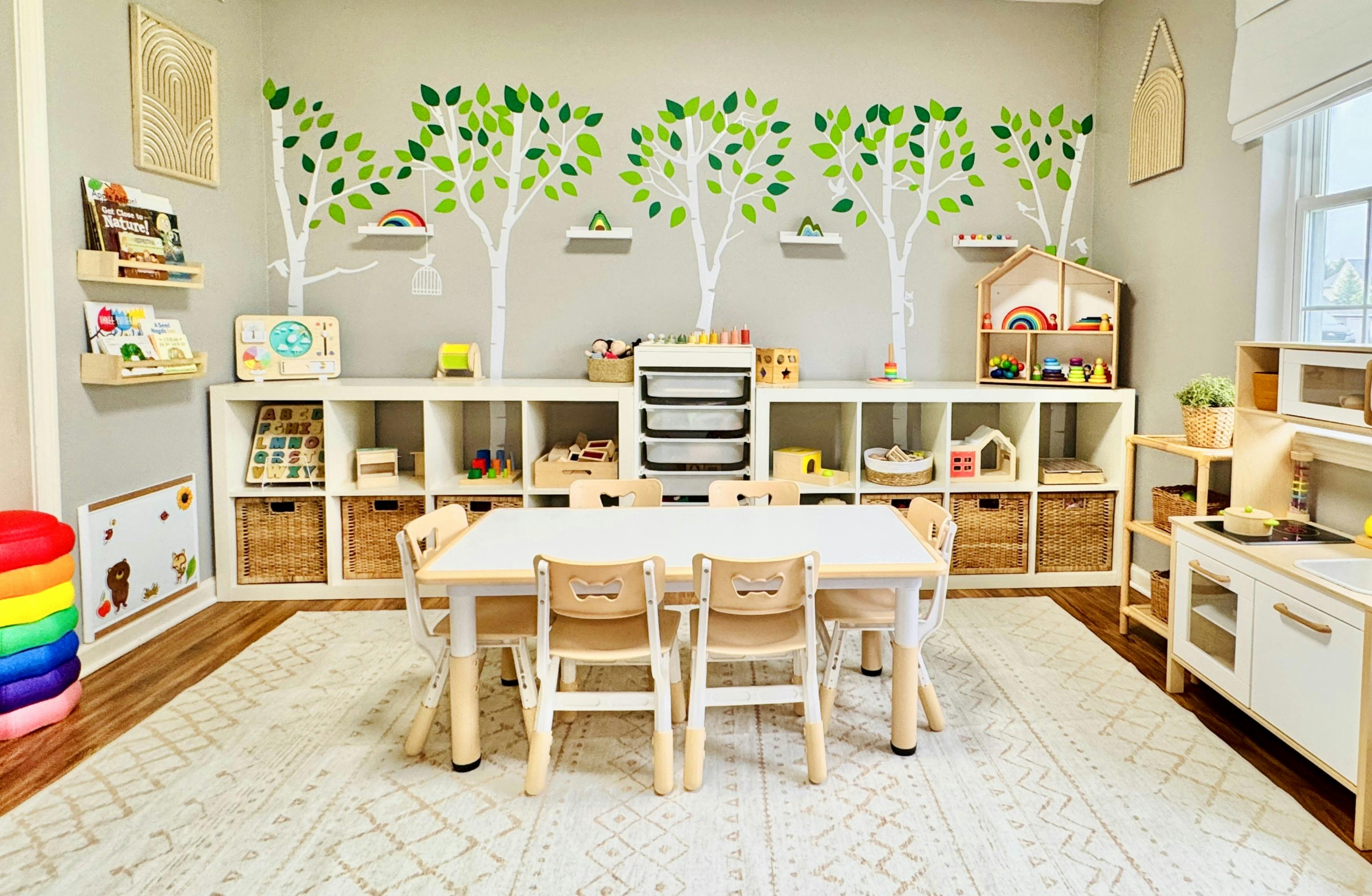 Playroom with a table and chairs, shelves with toys, and tree decals on the wall