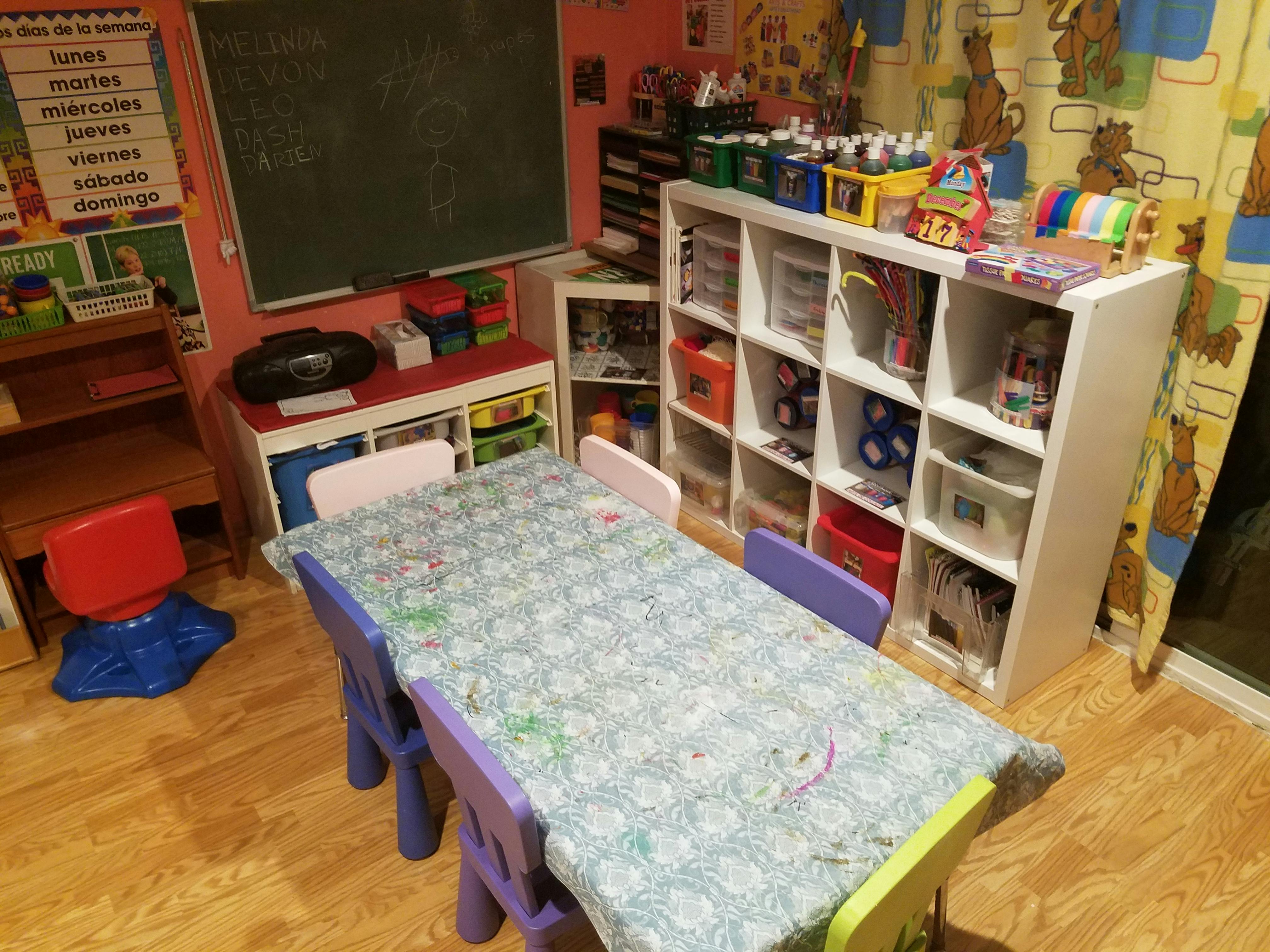 Classroom with a table and chairs, storage shelves, and a chalkboard