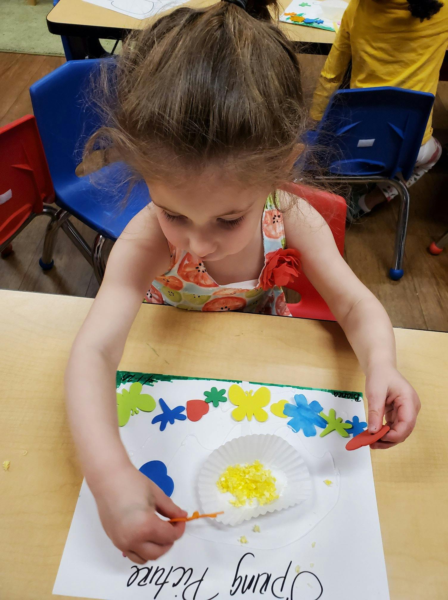Child creating art with paper cutouts and yellow sprinkles