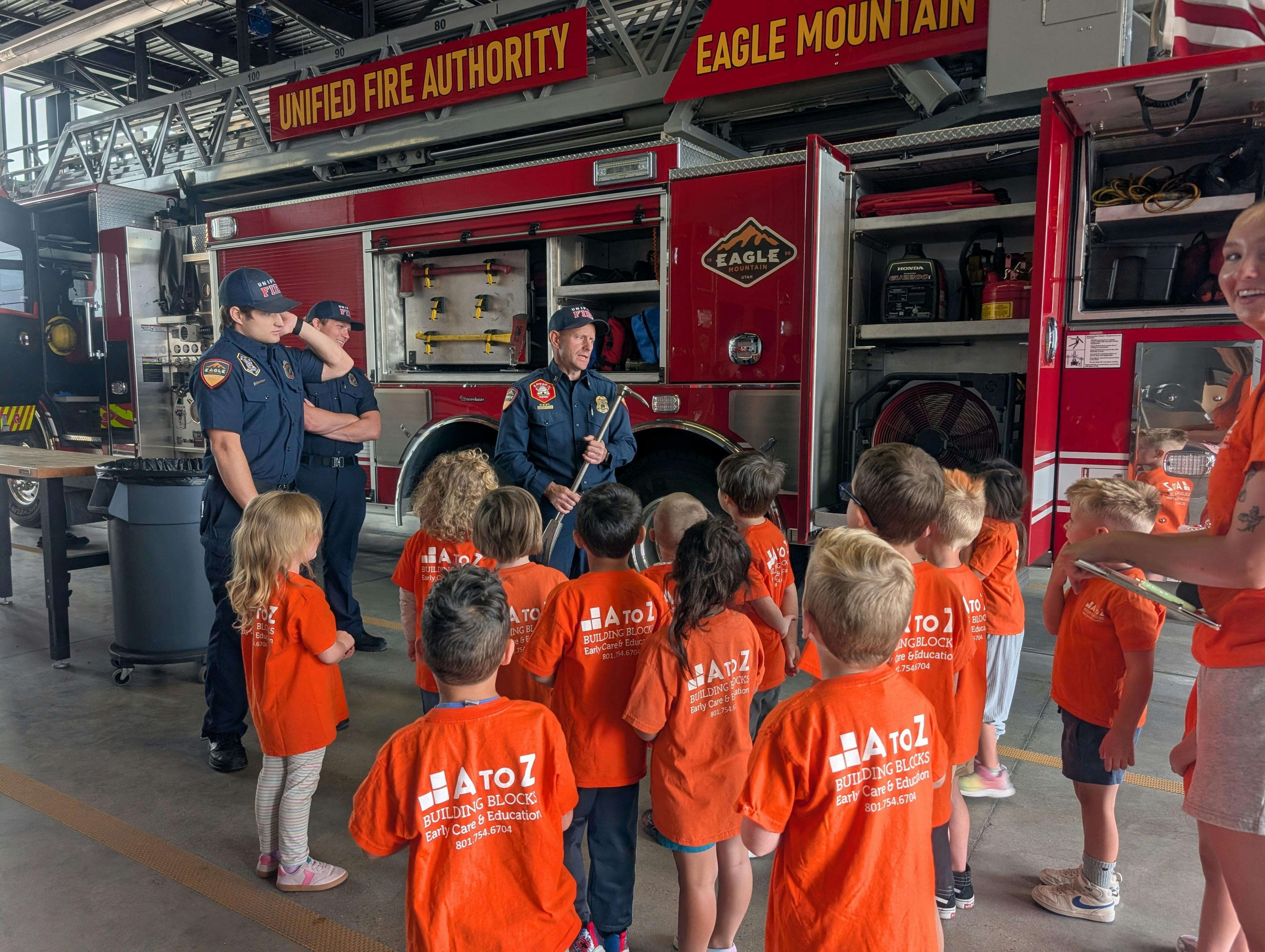 Firefighters in uniform talking to a group of children in a fire station
