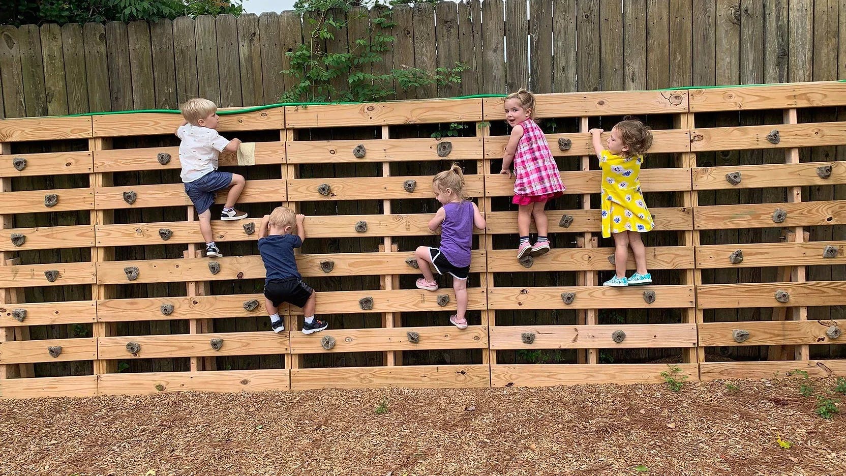 Multiple children climbing a wooden wall with handholds
