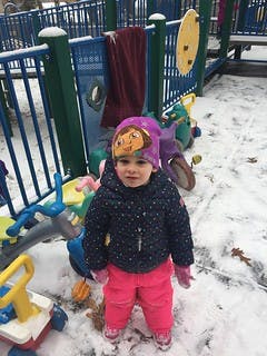 Child in winter clothing standing in snow near playground equipment