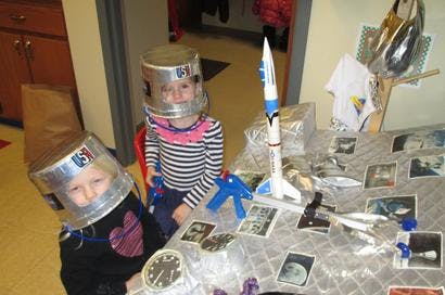 Two children wearing astronaut helmets playing with a toy rocket