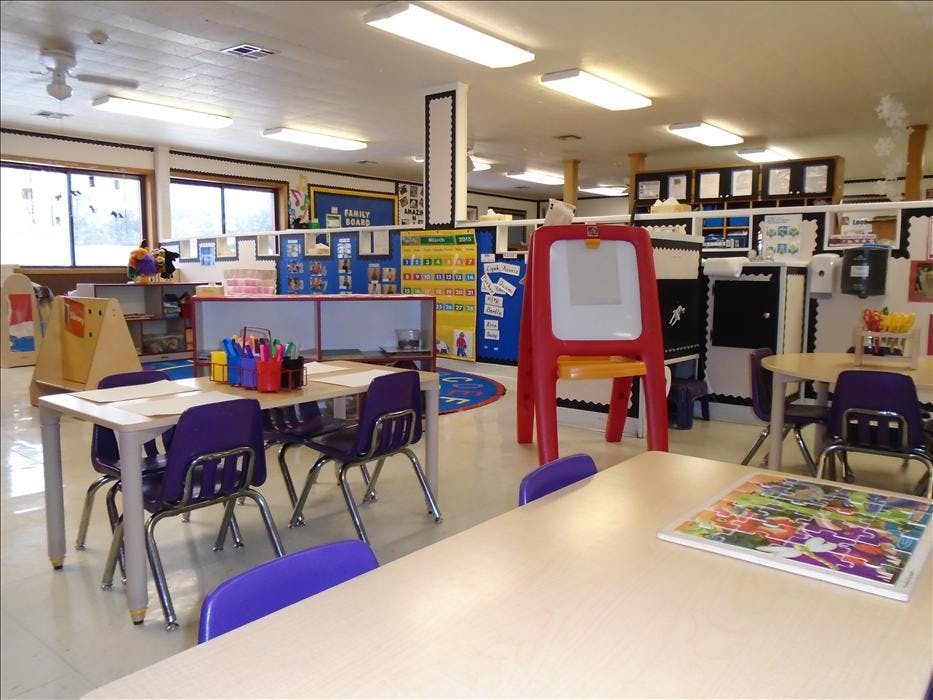 Empty classroom with small tables, purple chairs, and a red easel