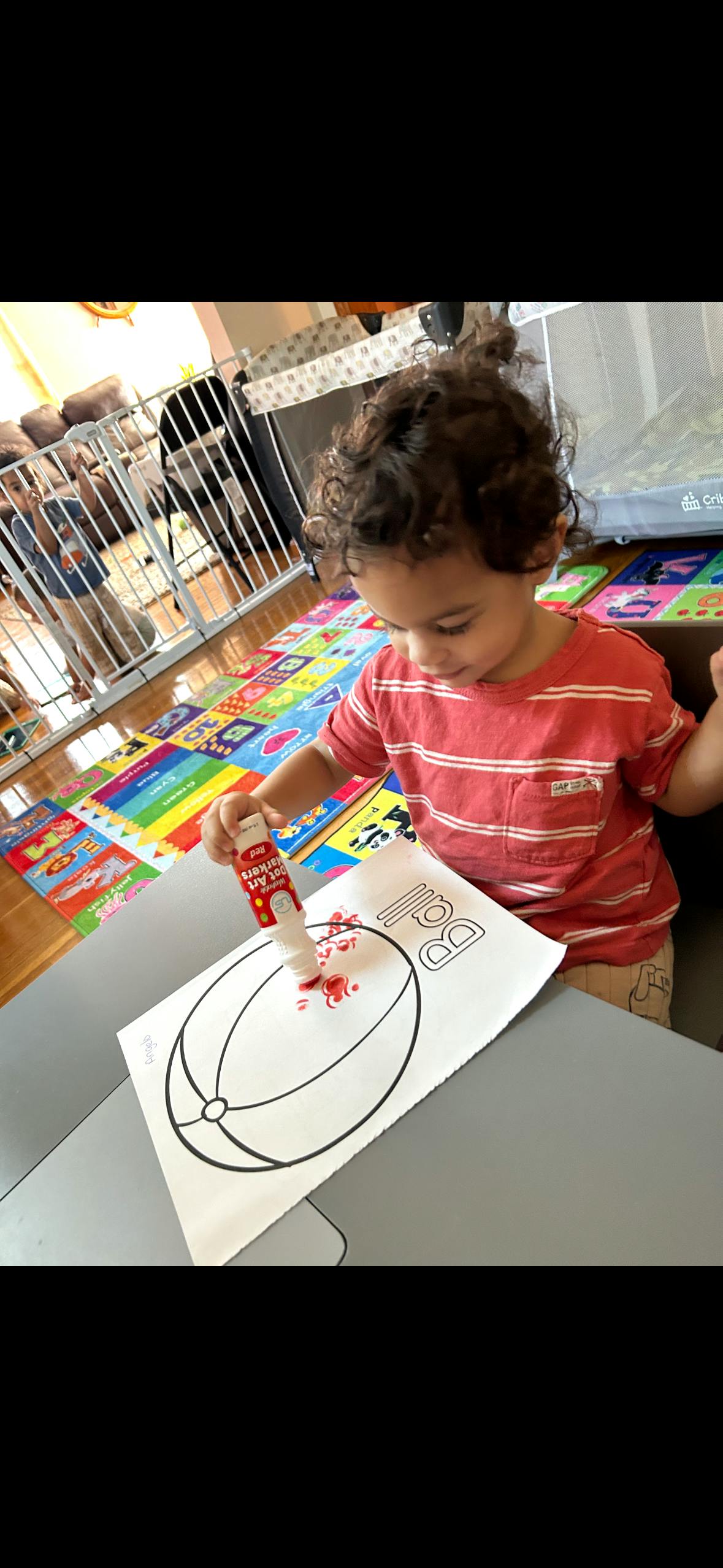 Child applying red dot art markers to a paper with an outline of a ball