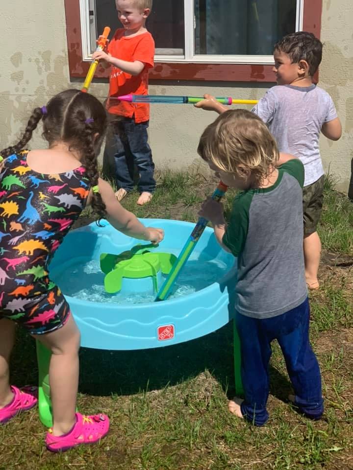 Children playing with water toys in a blue water table outdoors