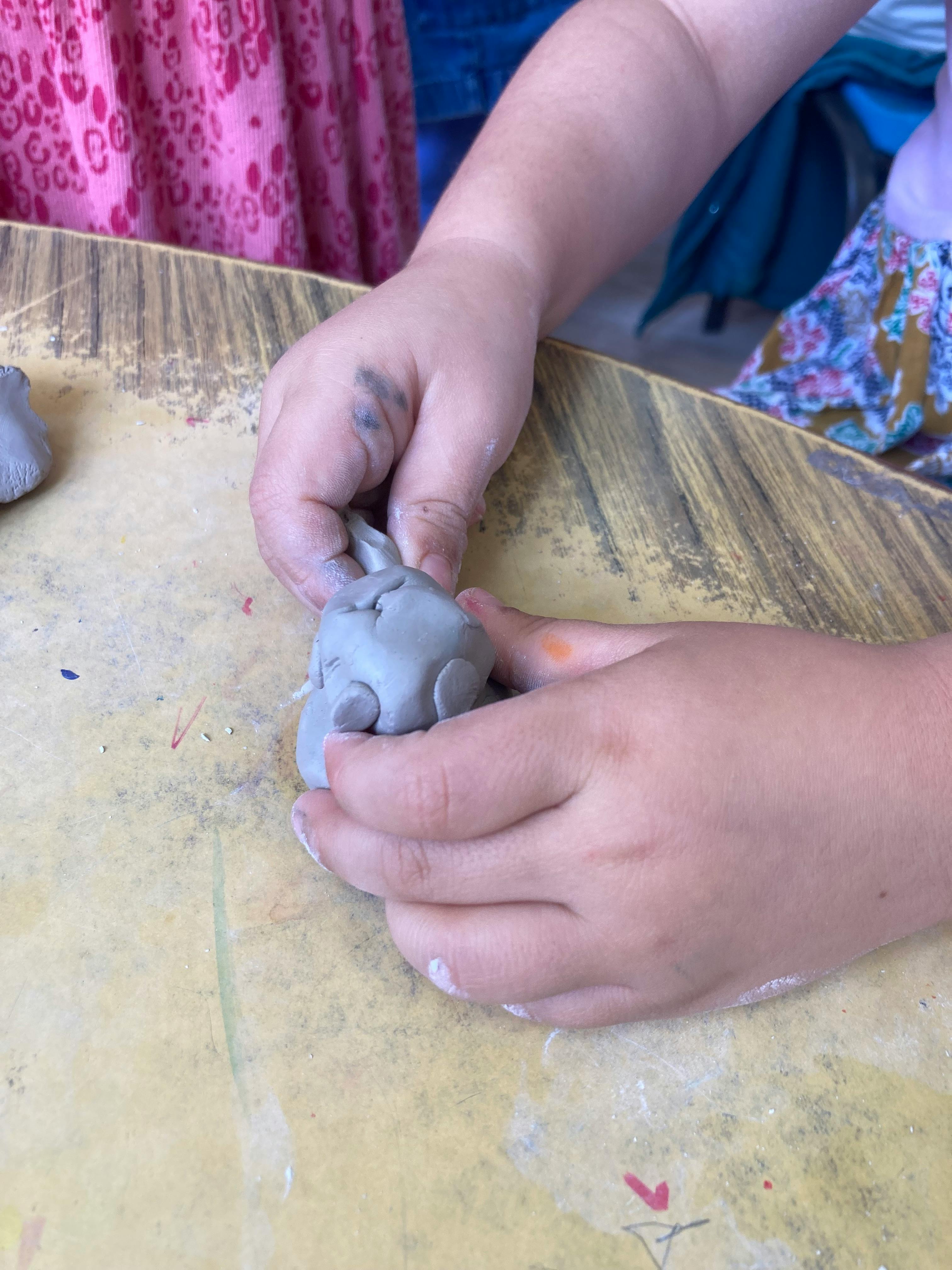 Child sculpting grey clay on a wooden table