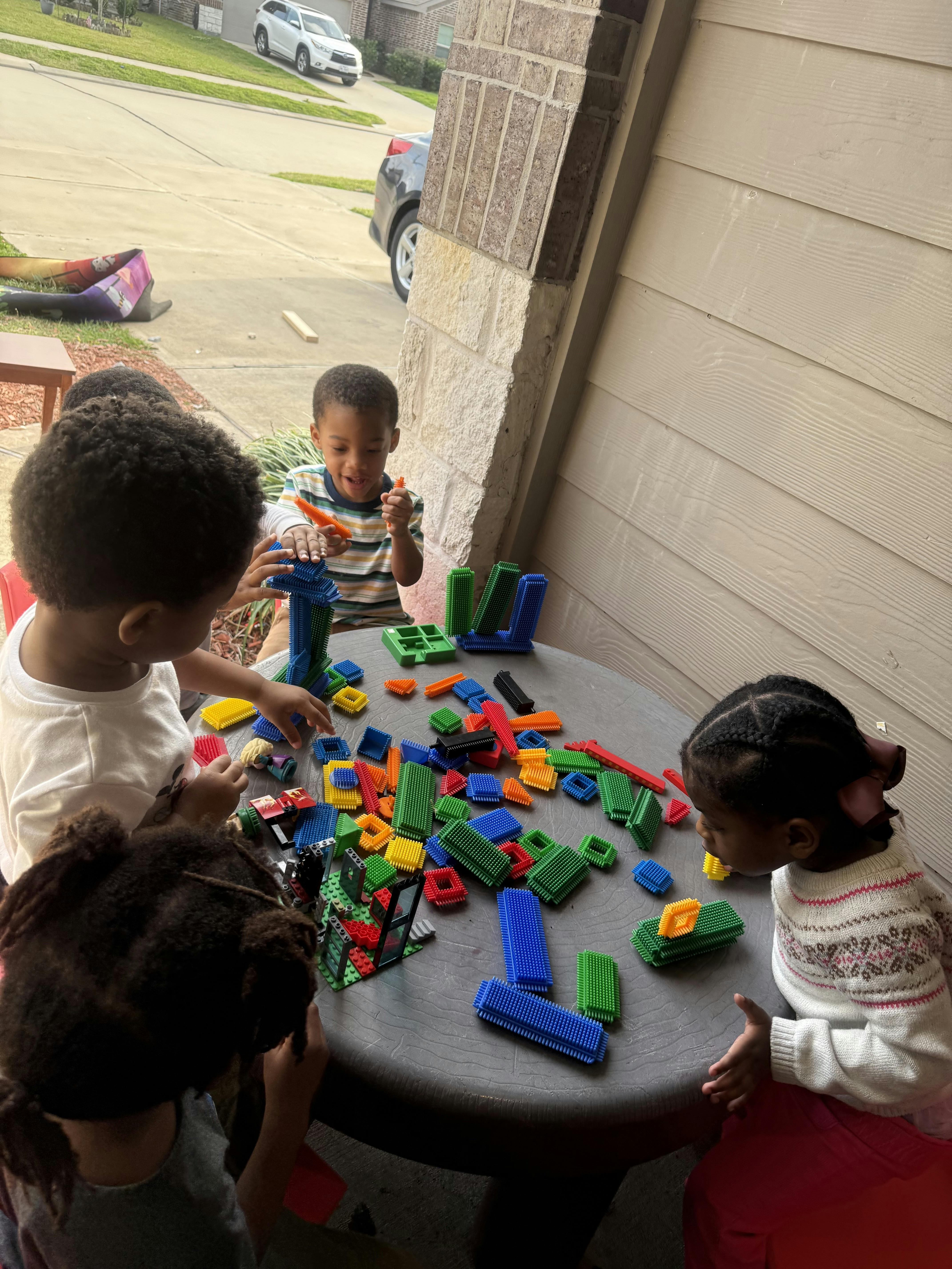 Three children playing with colorful interlocking building blocks on a table